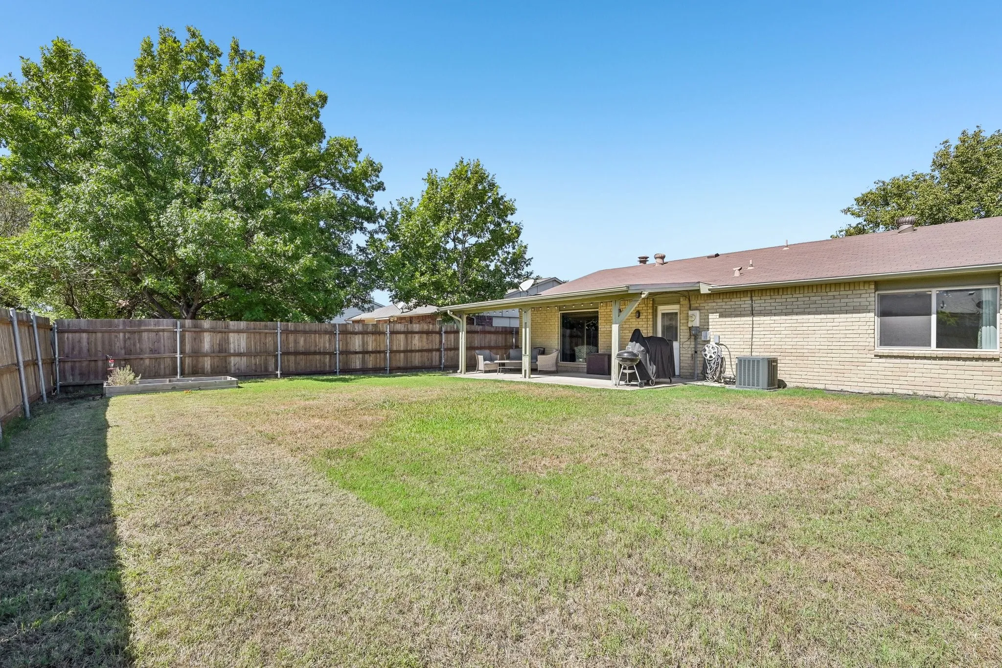 Expansive backyard featuring a wood-panel fence, mature trees, and a covered patio area