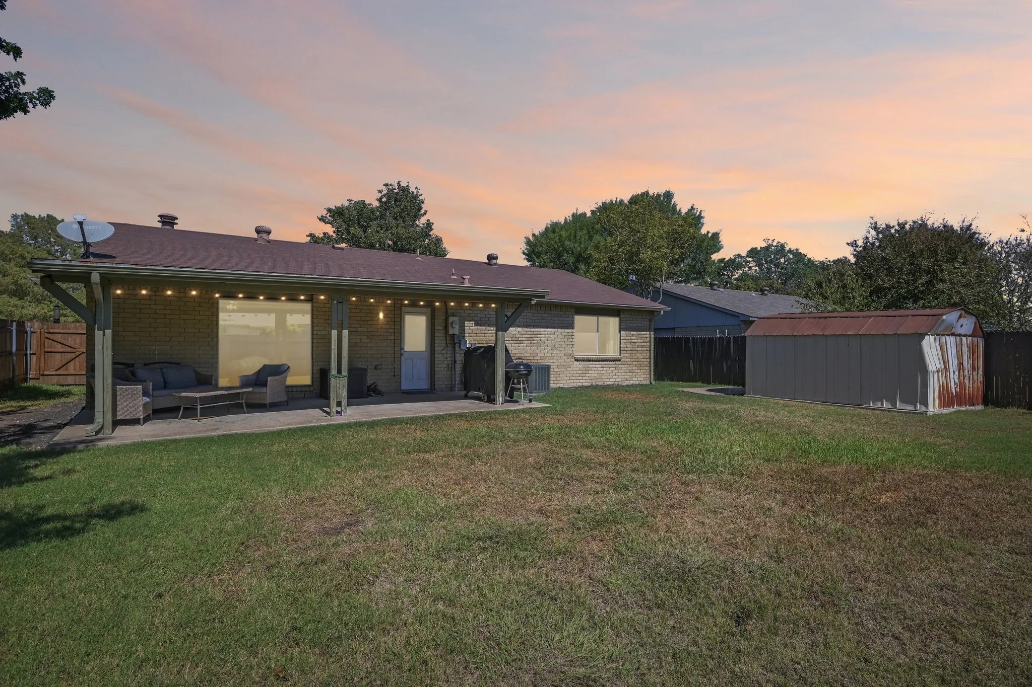 Expansive backyard with a covered patio, brick exterior, and a detached storage shed