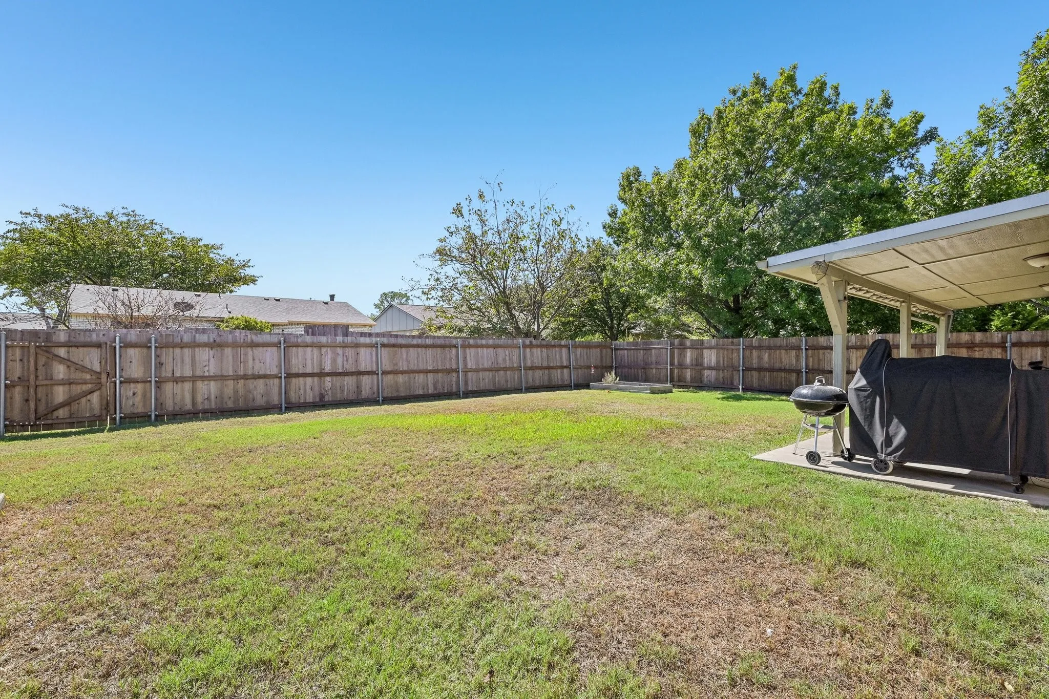 Expansive backyard featuring a wood fence, a covered patio, and a grass lawn