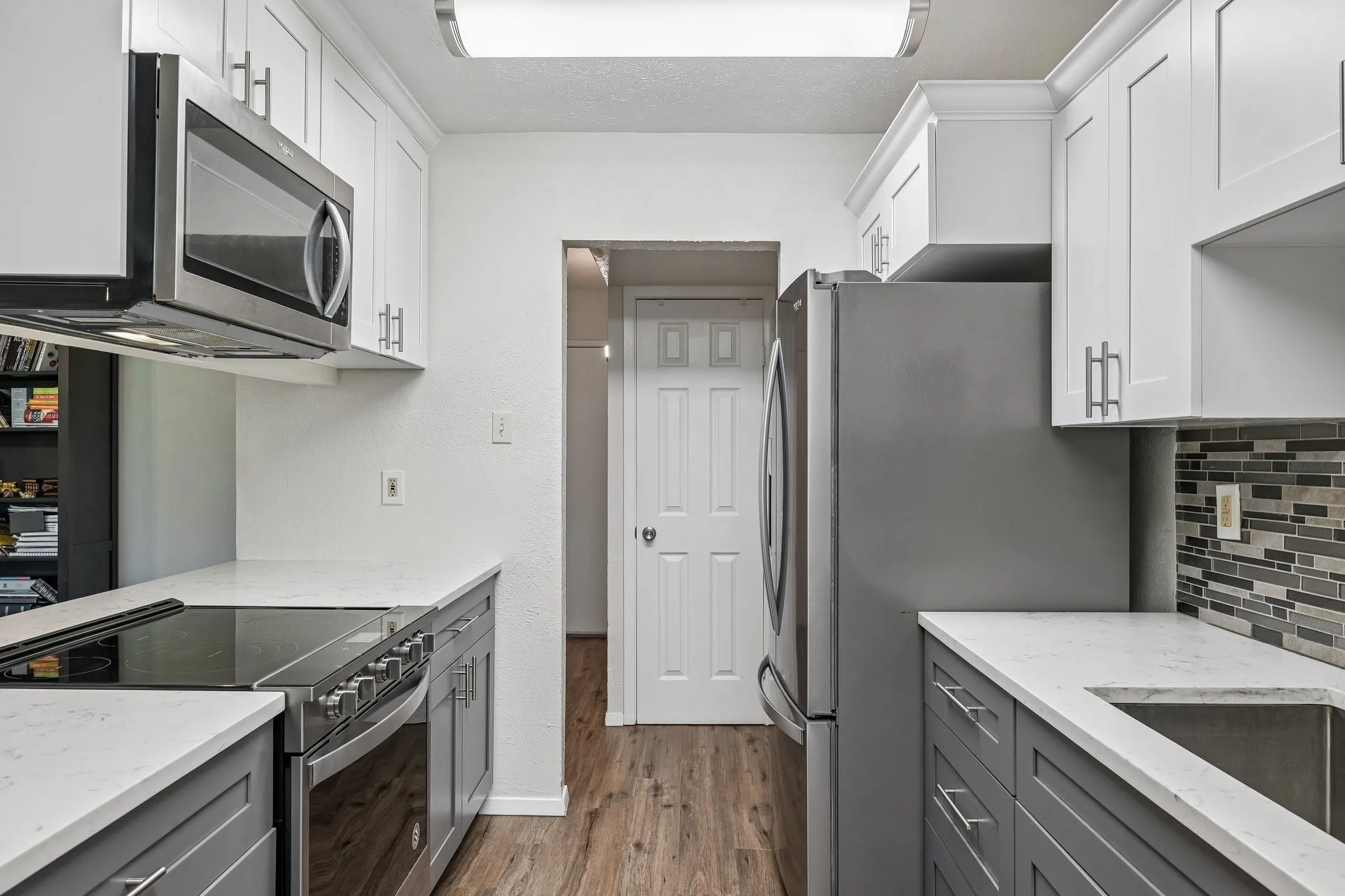 Kitchen featuring two-tone cabinetry with brushed nickel hardware, stainless steel appliances, white countertops, and wood-finish flooring