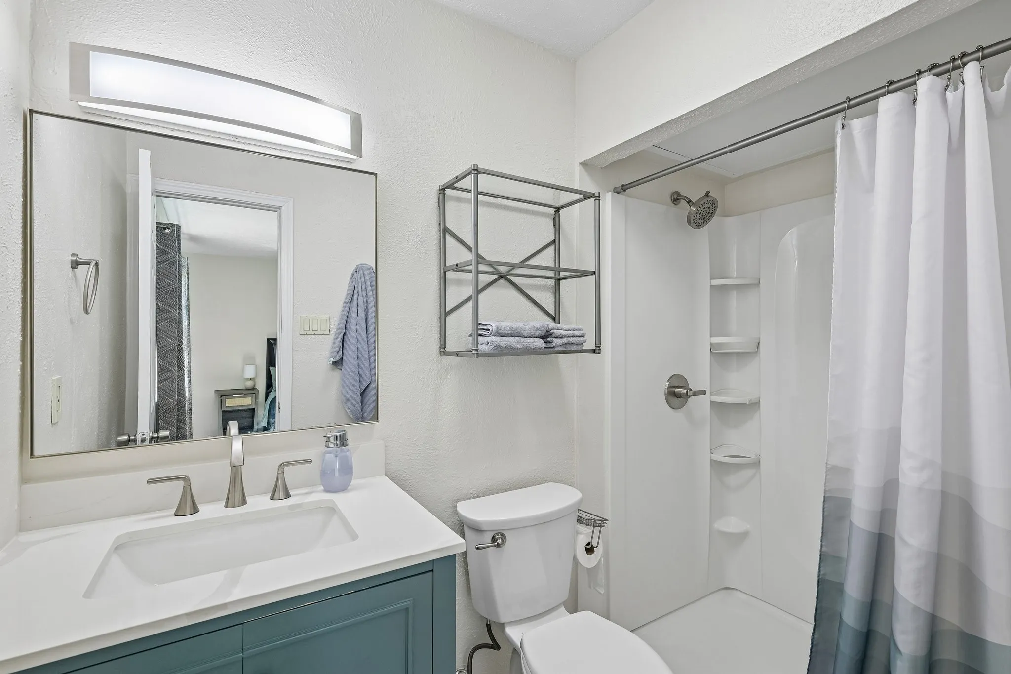 Bathroom featuring a single vanity with a white countertop, a white toilet, and a shower with built-in shelving