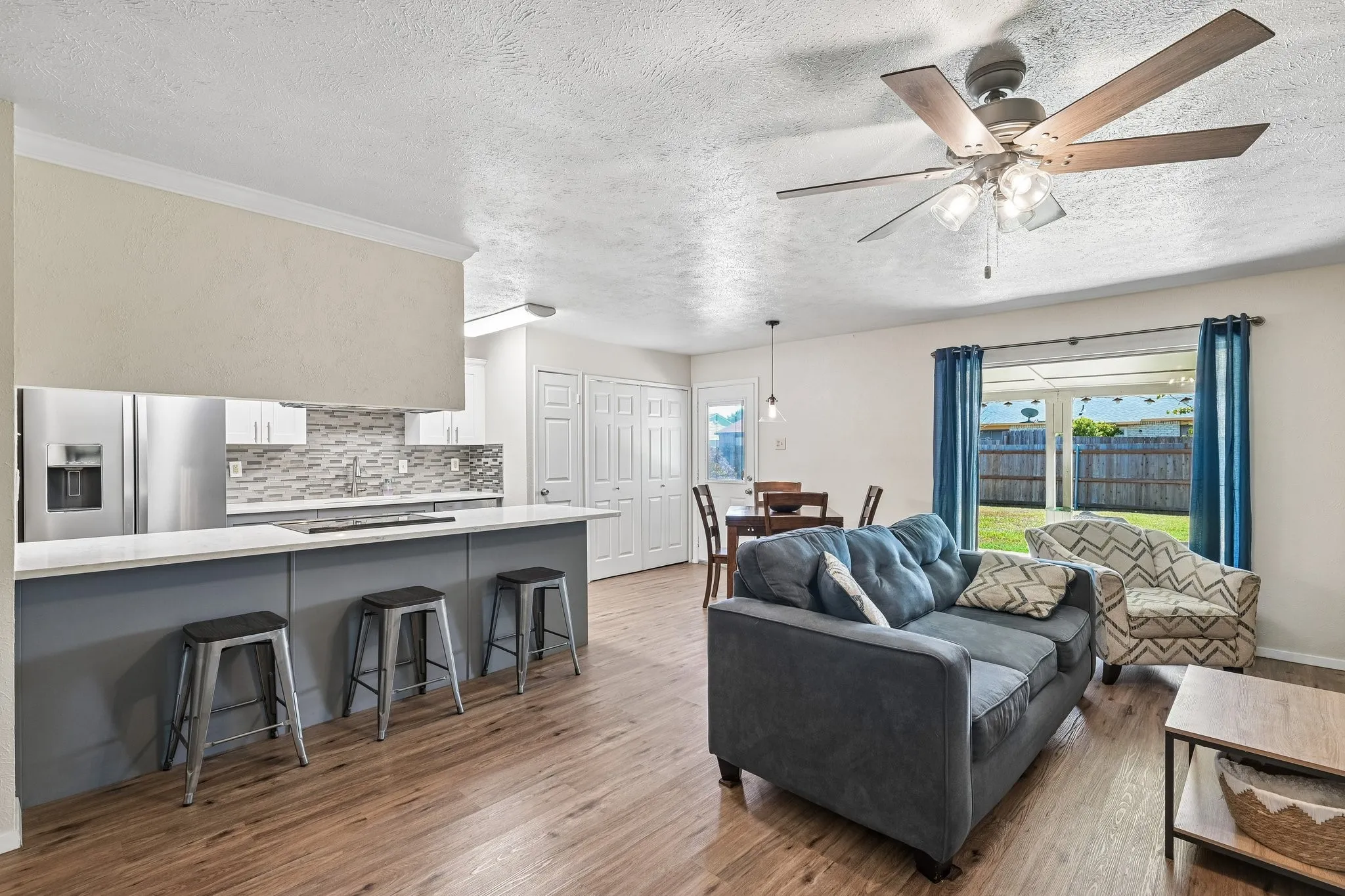 Wood-finish flooring, white cabinetry, stainless steel refrigerator, white countertops, and a ceiling fan with integrated lighting