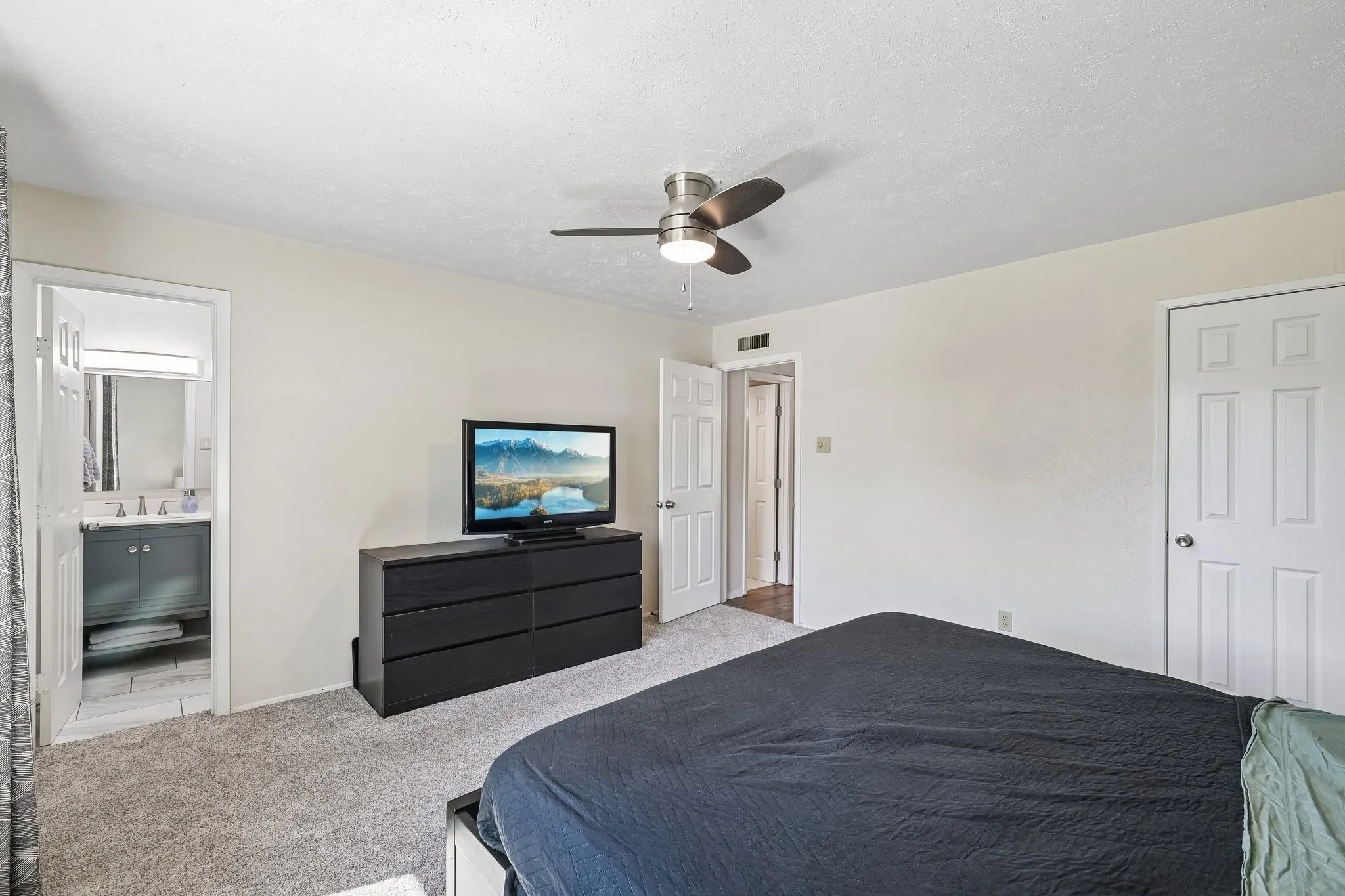 Plush carpeting, ceiling fan with integrated lighting, and an attached bathroom featuring a vanity with under-sink storage