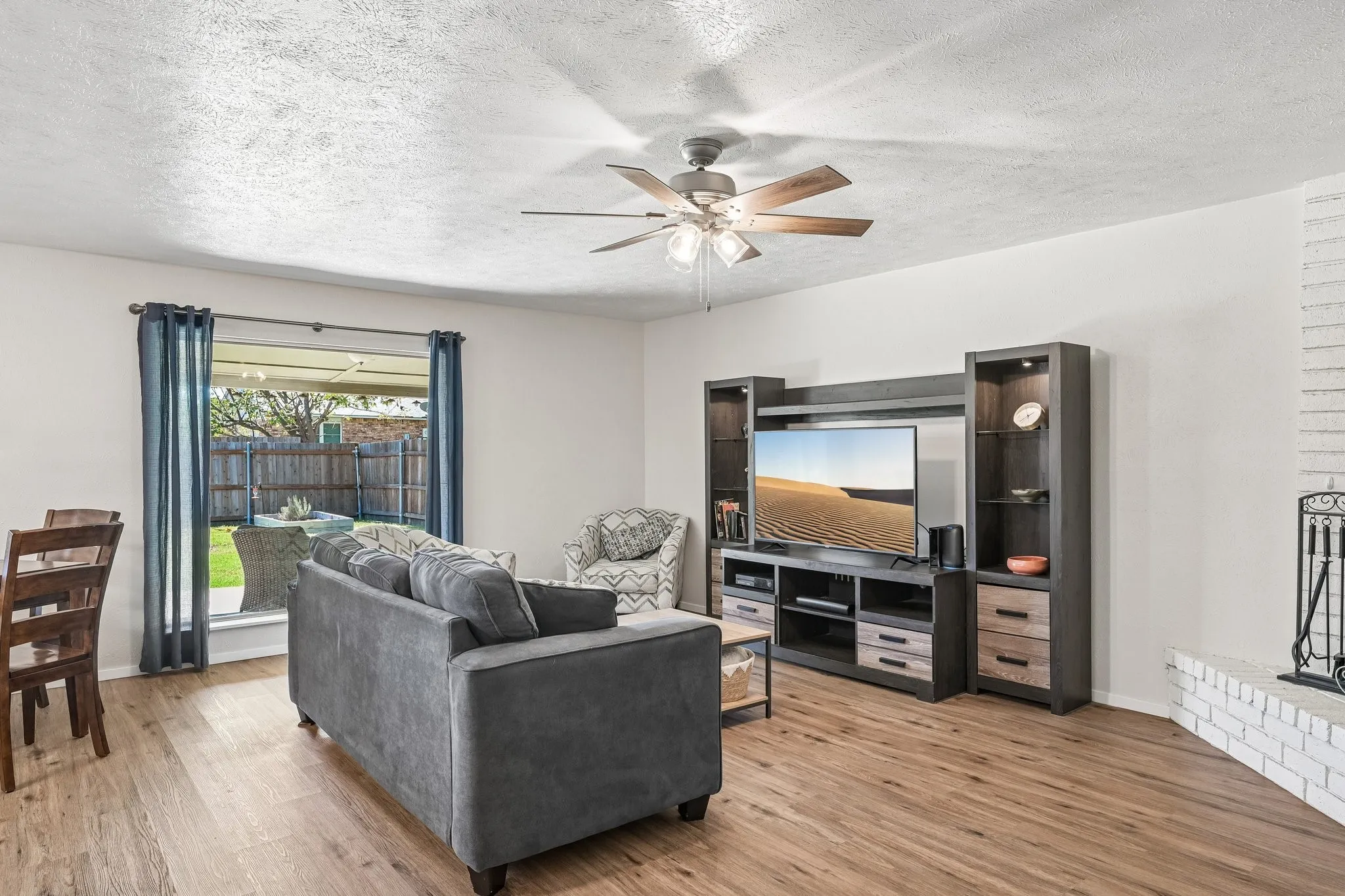 Wood-finish flooring throughout, a ceiling fan with light fixture, and a white brick fireplace