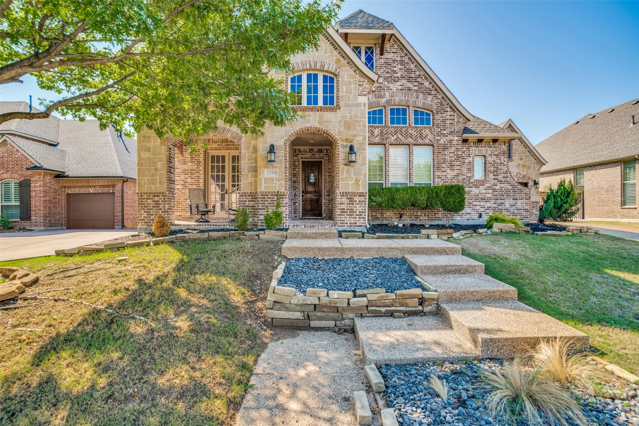 Stone and brick exterior with arched entry, multi-level concrete steps, and integrated landscaping