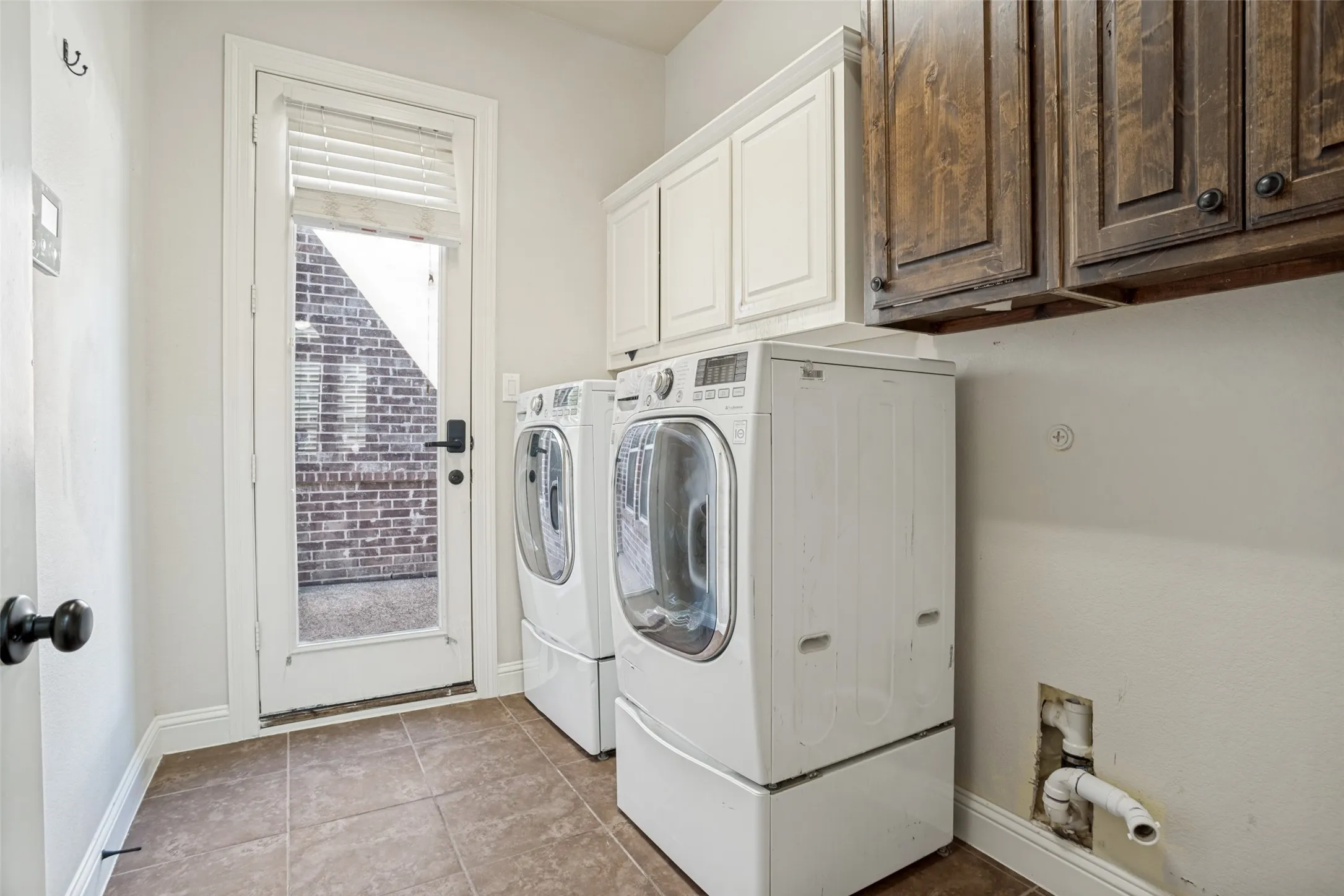 Laundry area featuring tile flooring, white upper cabinetry, and dark wood-finish upper cabinetry
