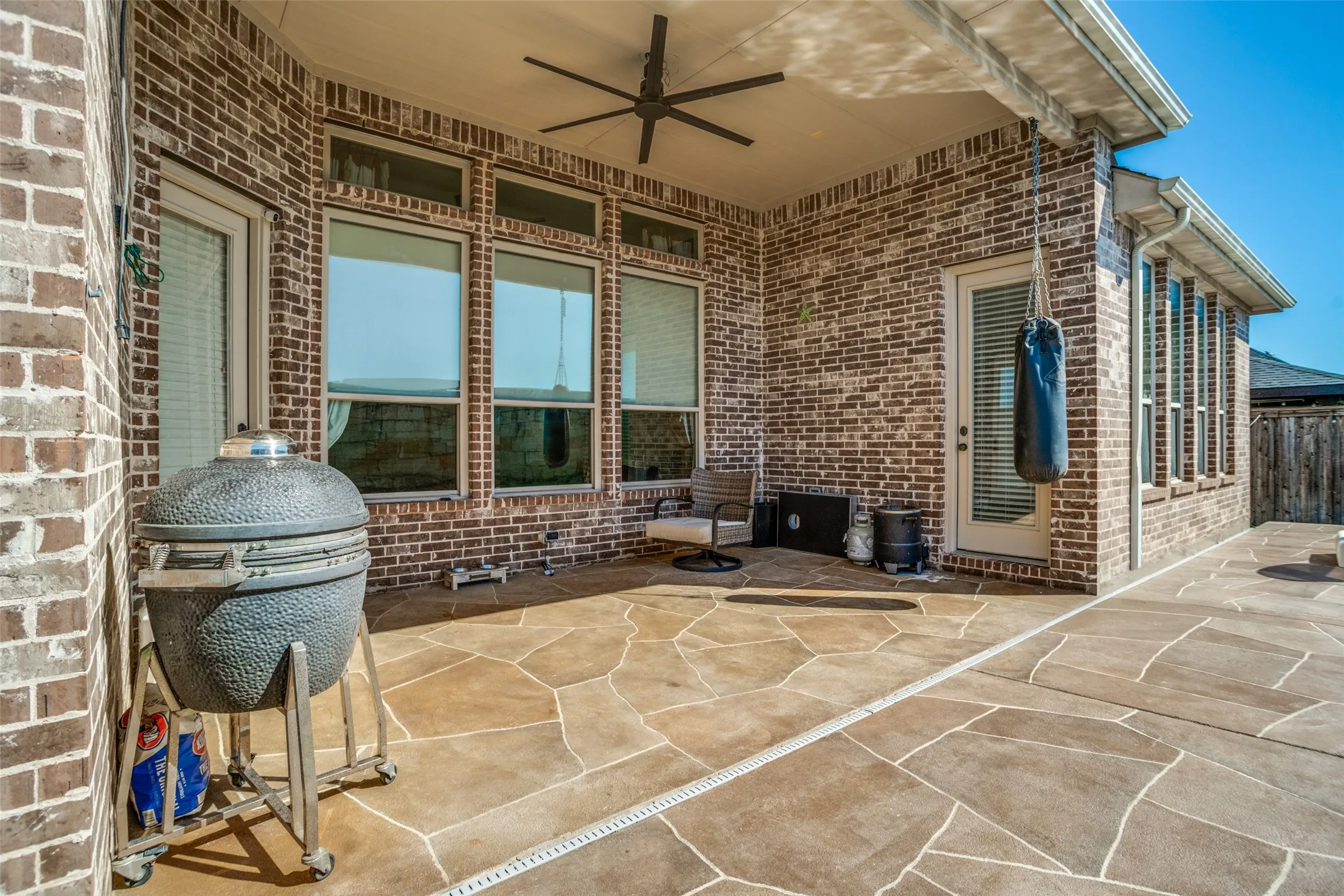 Covered patio featuring brick construction, a ceiling fan, multiple windows, and flagstone-patterned concrete flooring