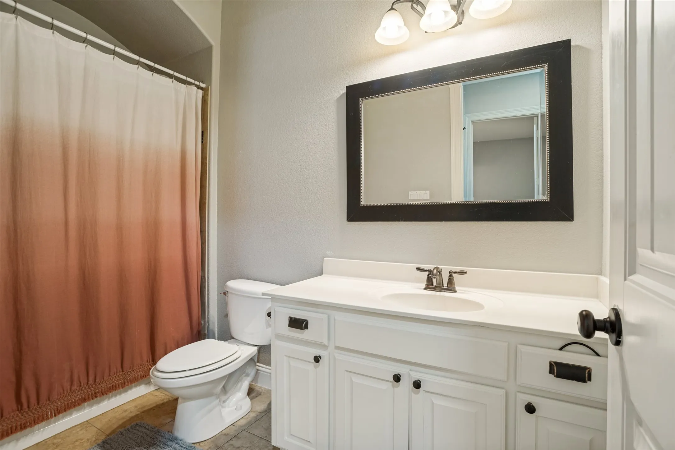 White cabinetry with black hardware, white countertop, framed mirror, and integrated sink