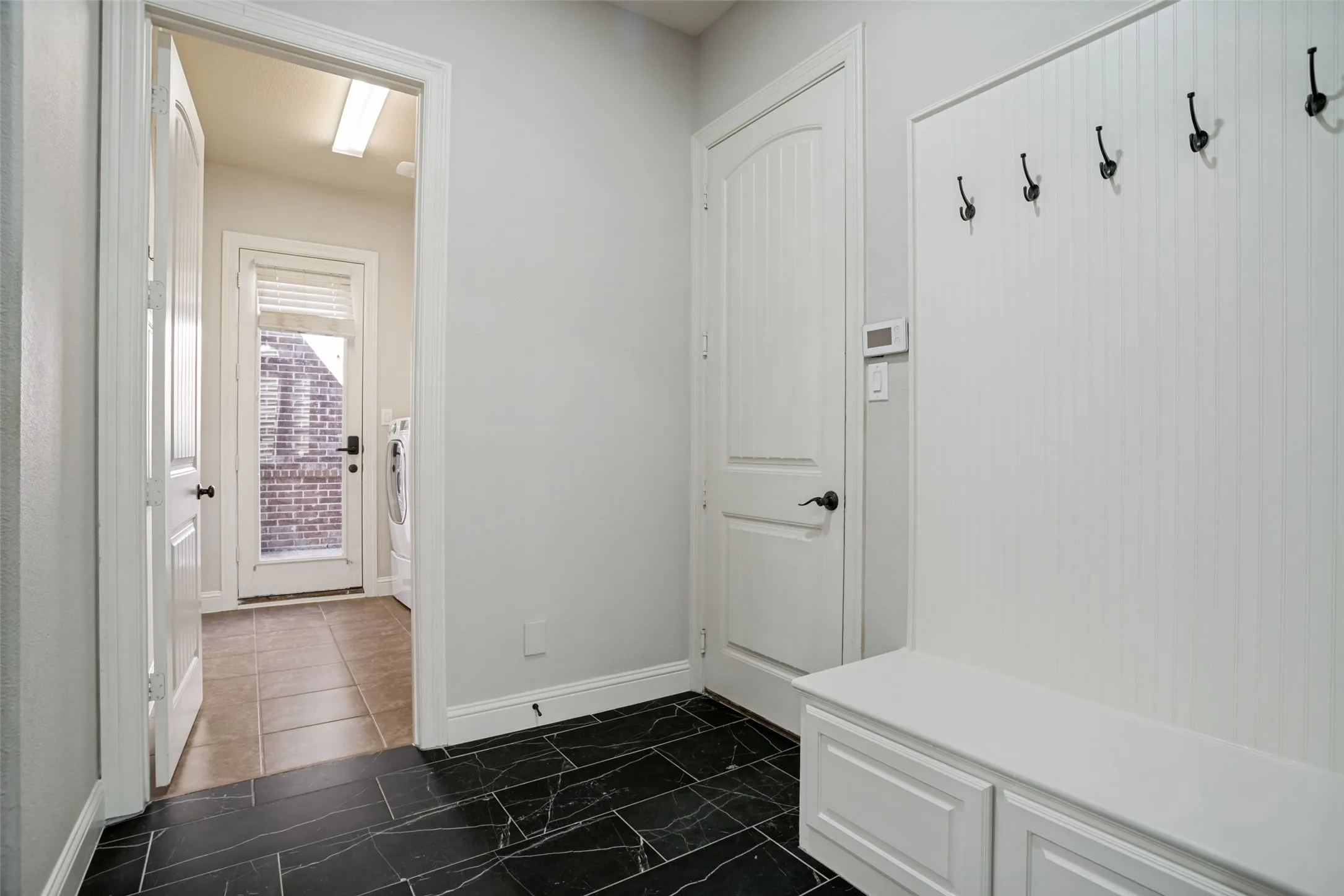 Built-in bench with storage, black tile flooring, white beadboard wall, and a full-light exterior door