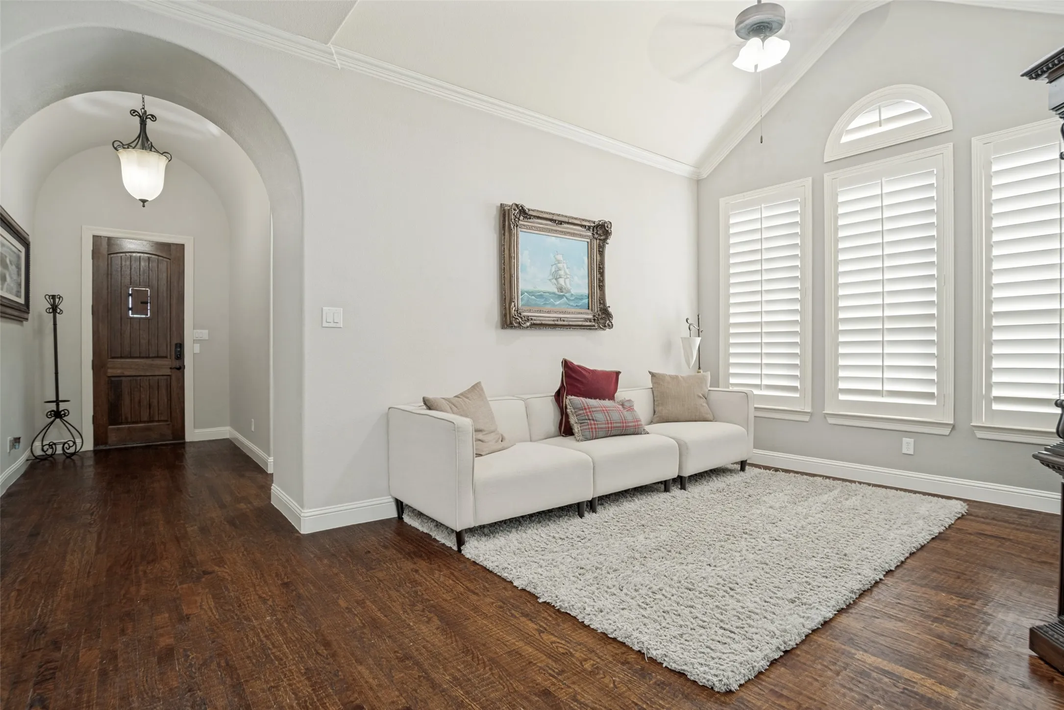 Vaulted ceiling with a ceiling fan, arched doorway, dark wood-finish flooring, and multiple windows with plantation shutters