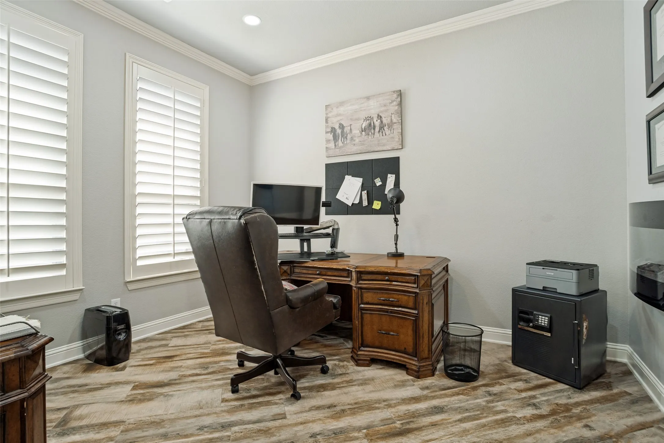 Light-toned walls with crown molding, two windows with white plantation shutters, and wood-finish flooring
