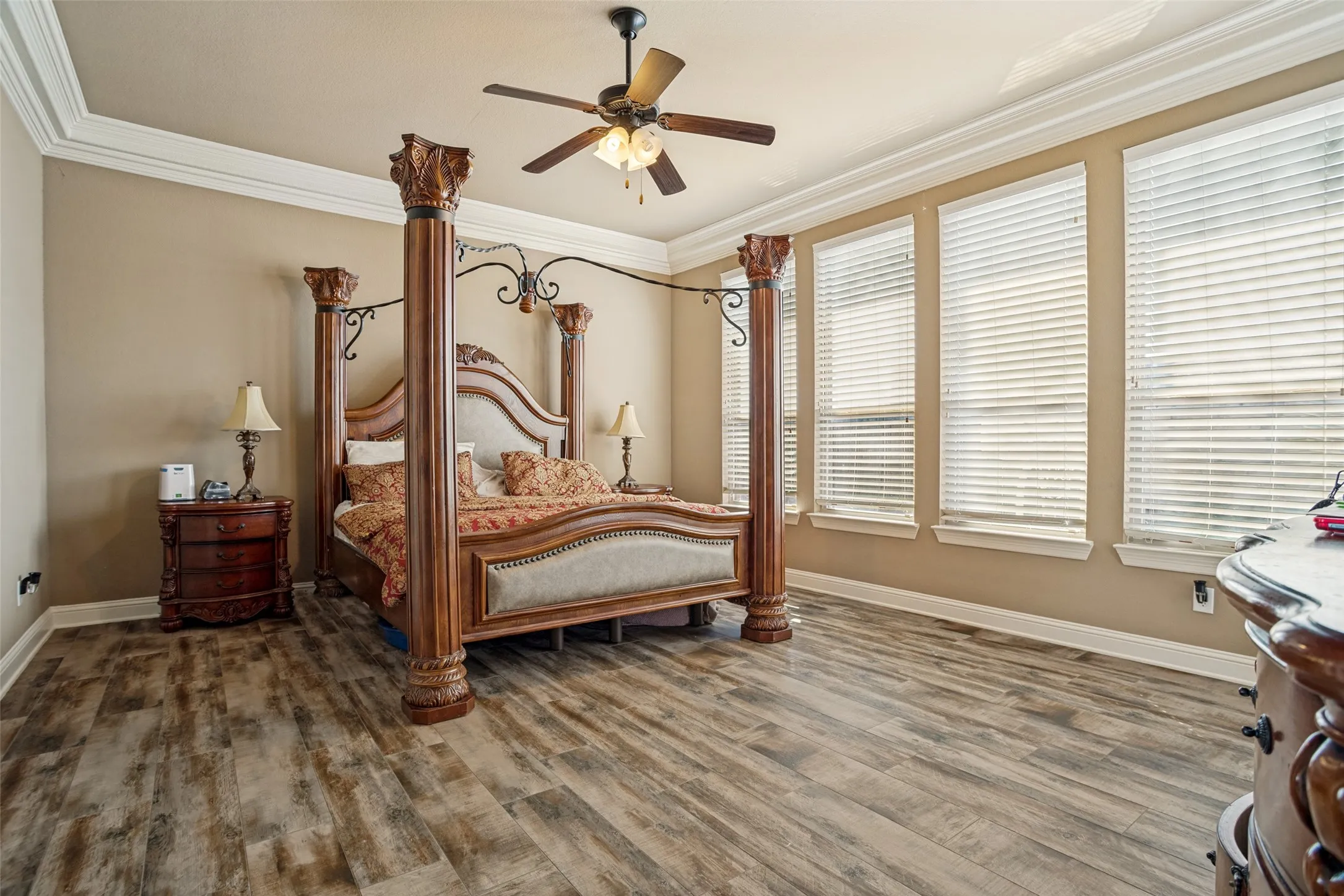 Wood-finish flooring, crown molding, ceiling fan, and multiple windows with blinds