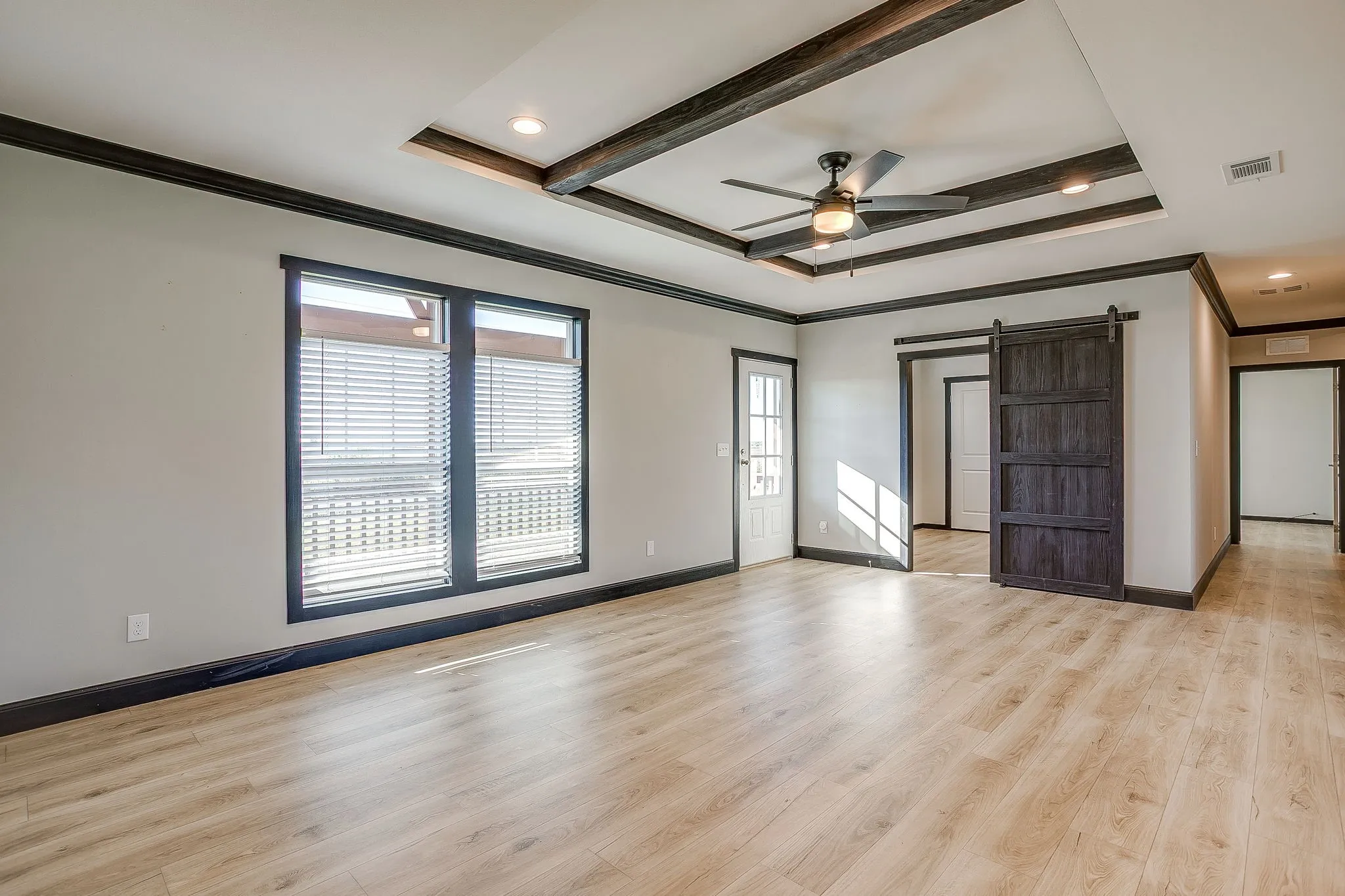 Tray ceiling with exposed wood-finish beams, recessed lighting, ceiling fan, wood-finish flooring, and a sliding barn door