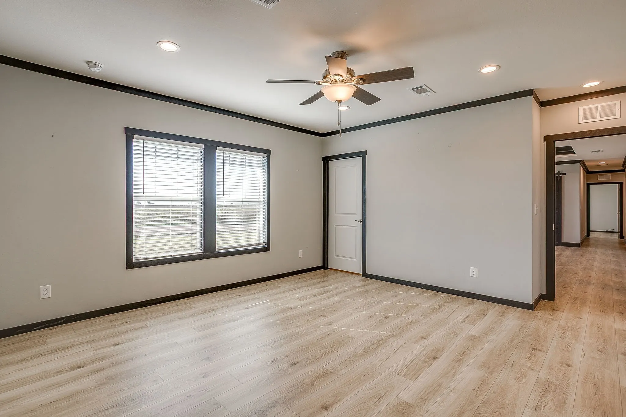 Recessed lighting, light wood-finish flooring, two large windows, dark trim, and a ceiling fan with integrated lighting
