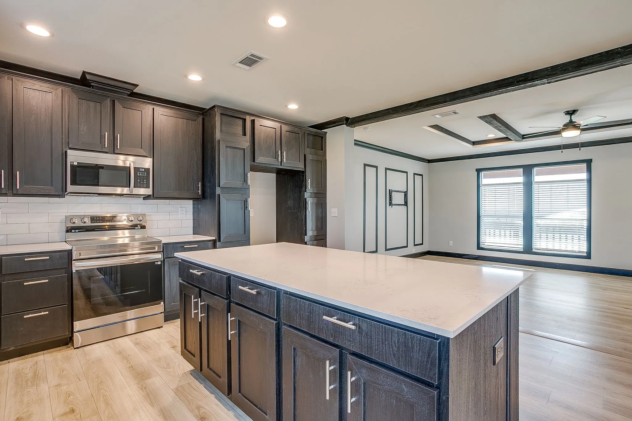 Kitchen featuring dark wood-finish cabinetry, stainless steel appliances, white subway tile backsplash, and a large central island with a light-toned countertop