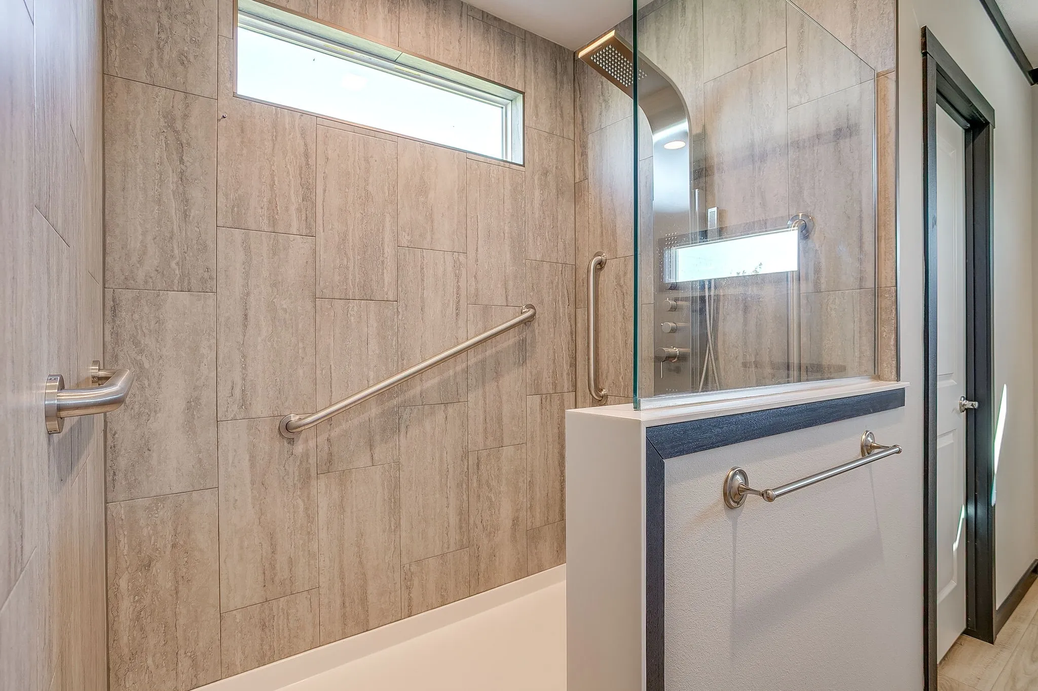 Walk-in shower with full-height tile surround, fixed glass panel, and multiple grab bars