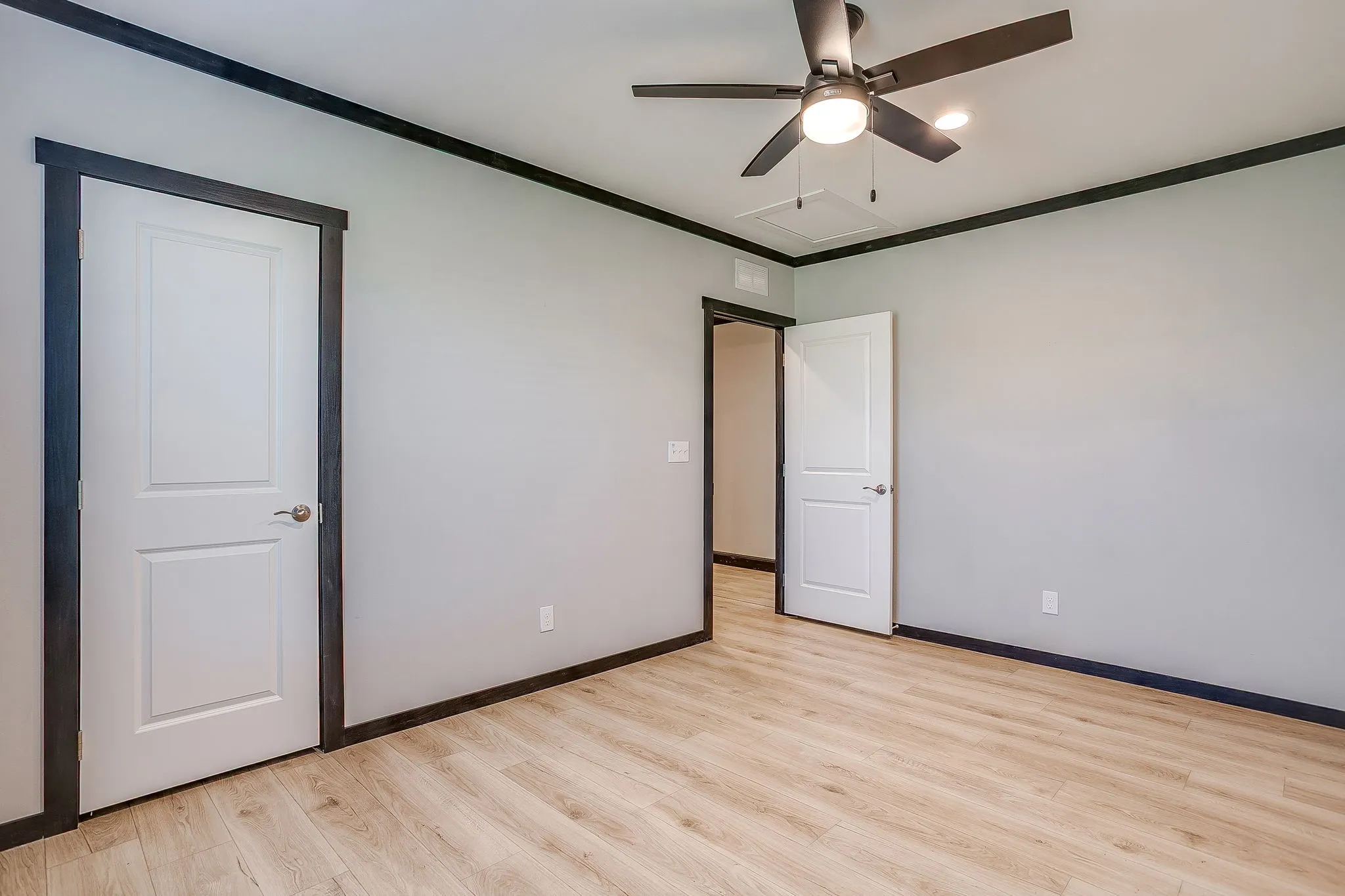 Light wood-finish flooring, a ceiling-mounted fan with integrated lighting, and white interior doors with dark trim