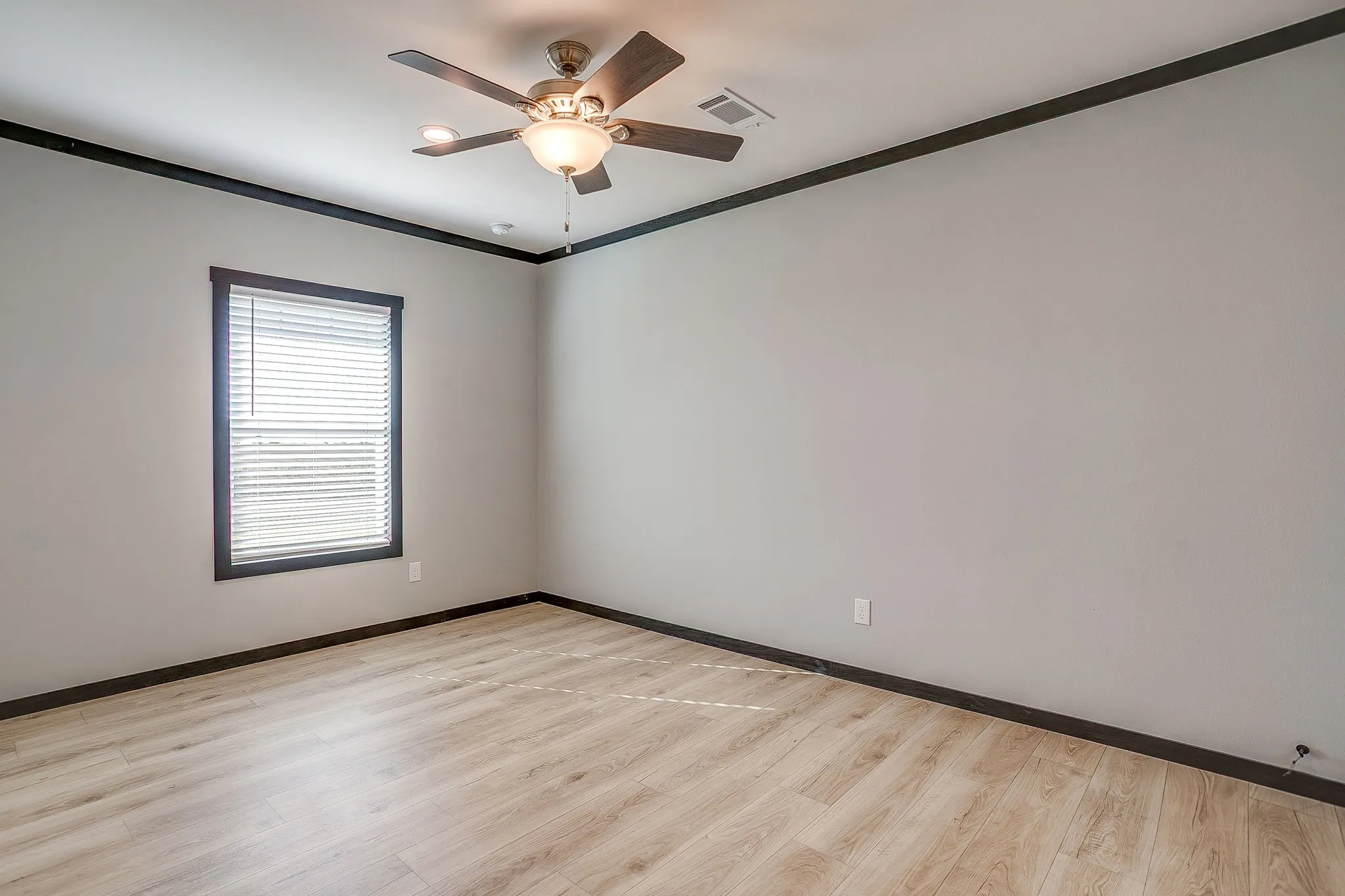 Wood-finish flooring, ceiling fan with integrated lighting, window with blinds, dark trim accents, and light gray walls