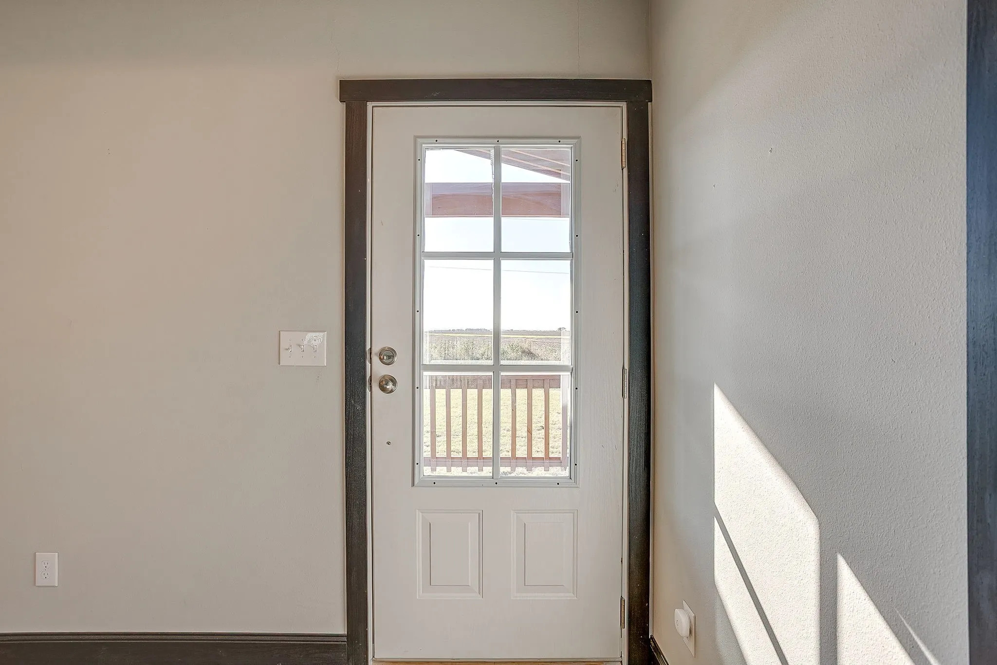 White paneled door with integrated window panels, dark wood-finish trim, and a visible exterior railing