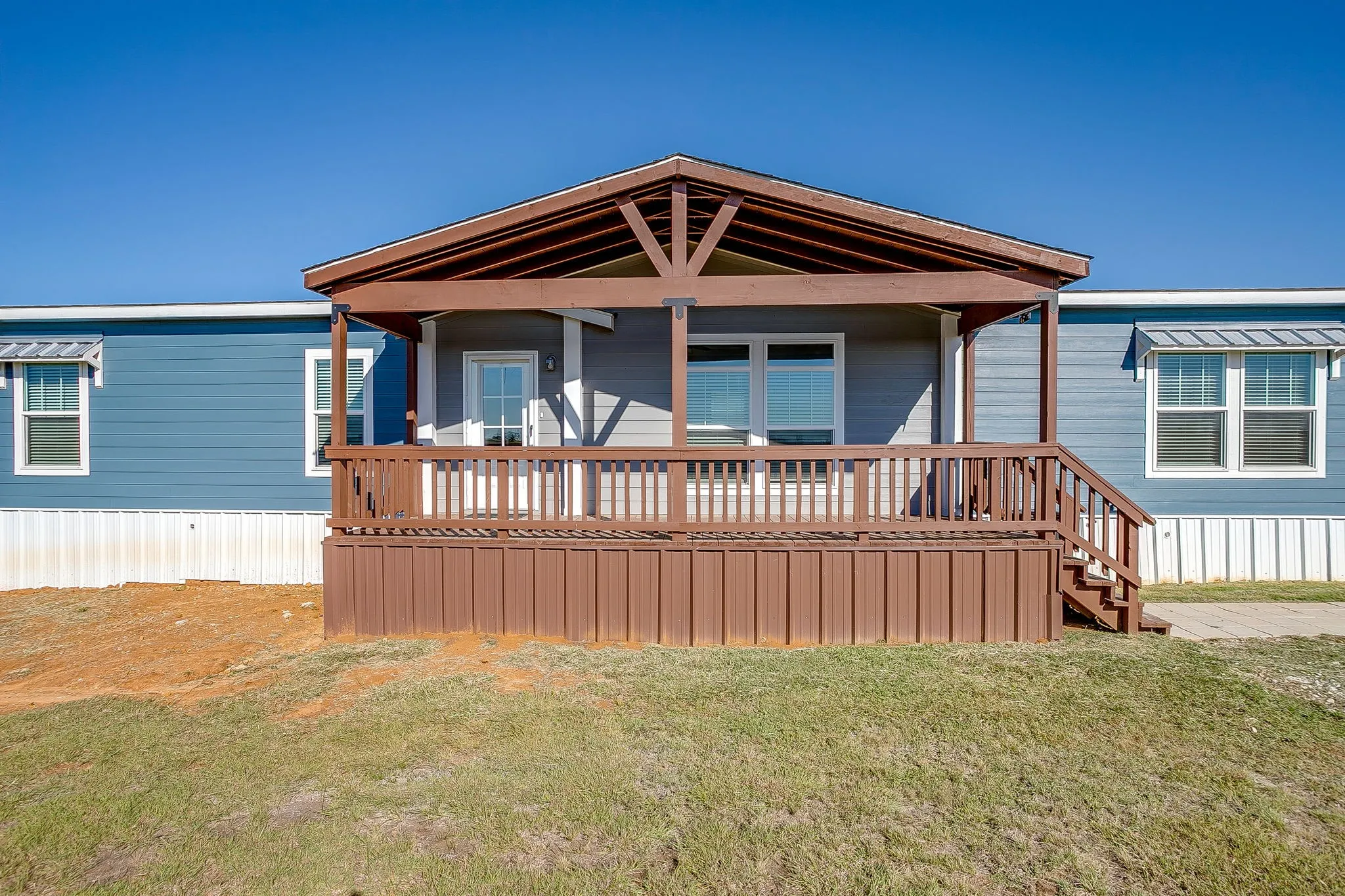 Covered front porch with wood railings and steps, featuring blue siding and white window awnings