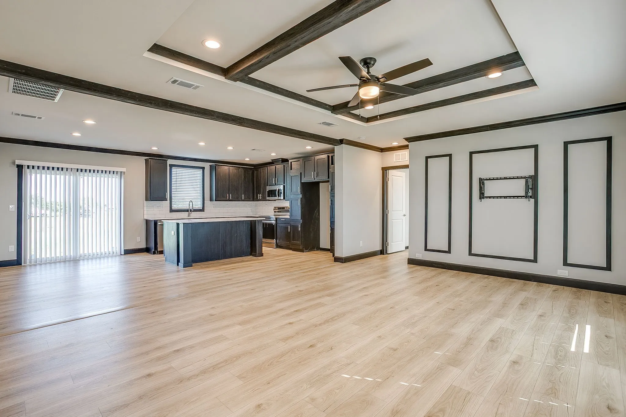 Recessed lighting, wood-finish flooring, tray ceiling with exposed dark wood beams, built-in ceiling fan, and a kitchen island with seating