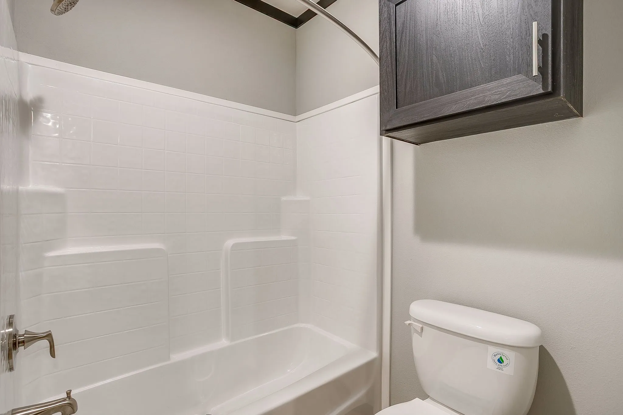 Tub and shower combination with a brushed nickel shower head and fixtures, a white toilet, and a dark wood-finish wall-mounted cabinet