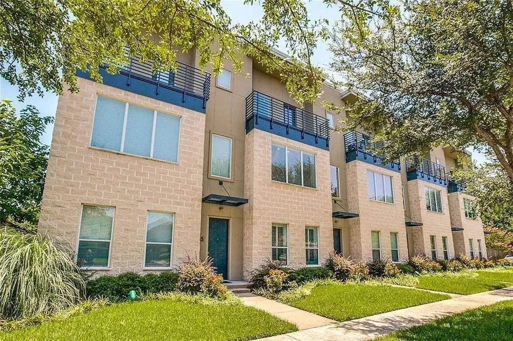 Contemporary exterior featuring light brick masonry, multiple balconies with metal railings, a modern entry awning, and manicured landscaping