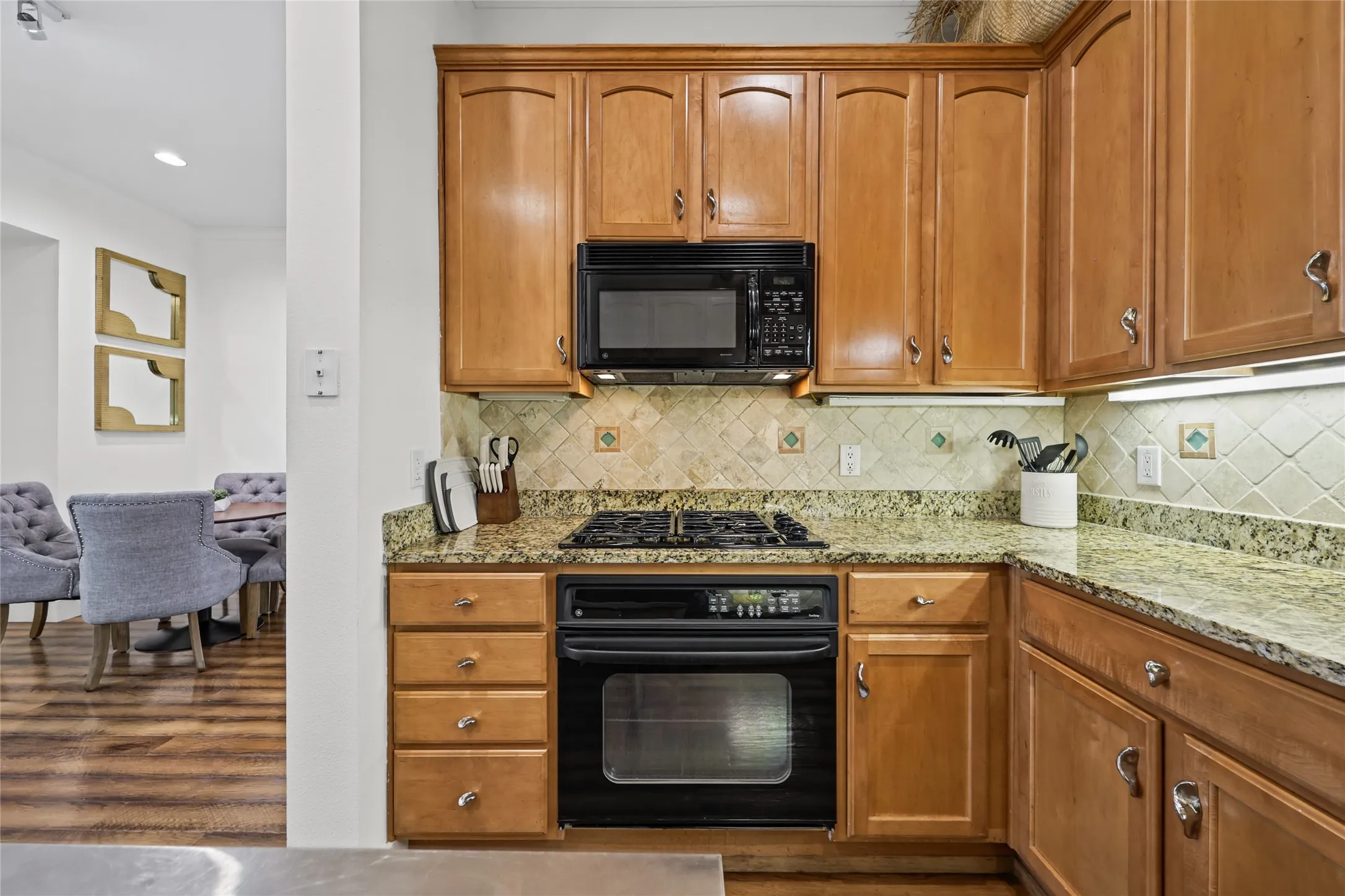 Warm wood cabinetry with ample storage and brushed nickel hardware, granite countertops, and a coordinating tile backsplash