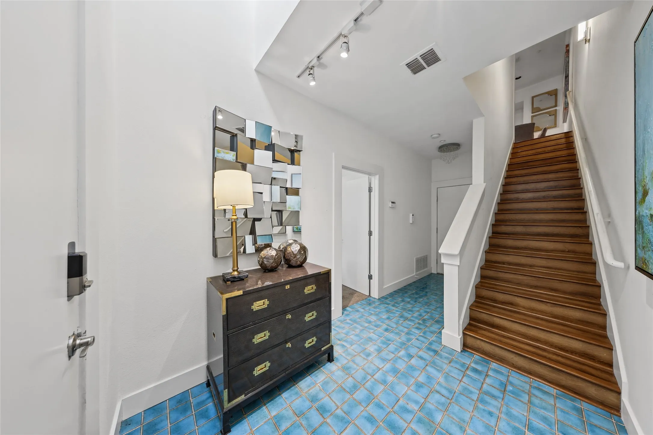 Two-story foyer featuring blue square tile flooring, wood stairs with white risers, white painted walls, and track lighting