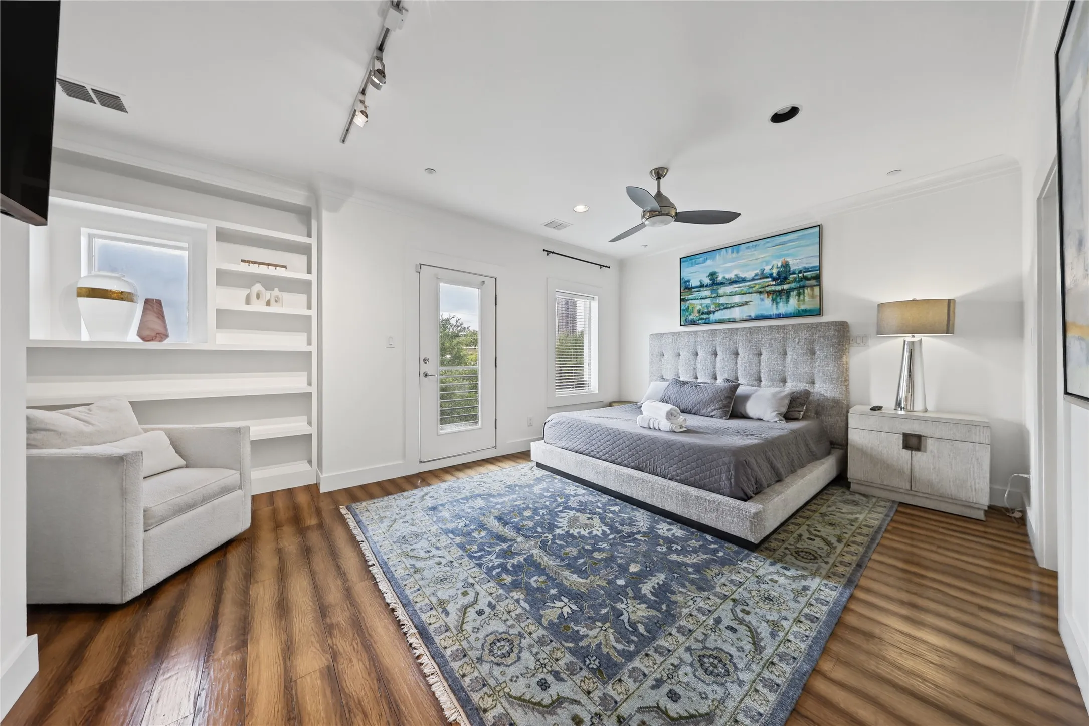Wood-finish flooring, built-in shelving, white walls, and a ceiling fan with integrated lighting