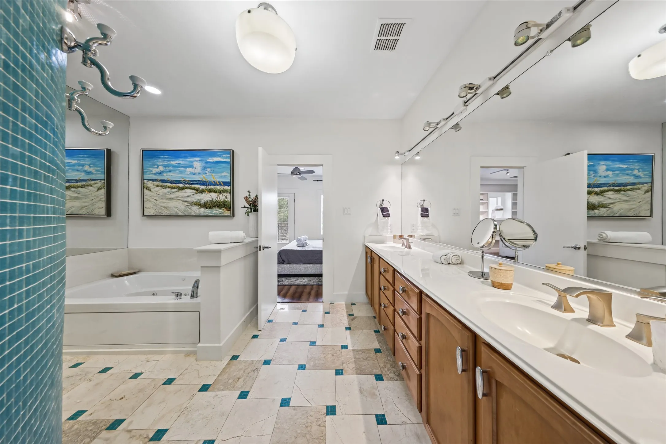 Dual vanity with undermount sinks and brushed nickel fixtures, wood-finish cabinetry, track lighting, corner soaking tub, and patterned tile flooring