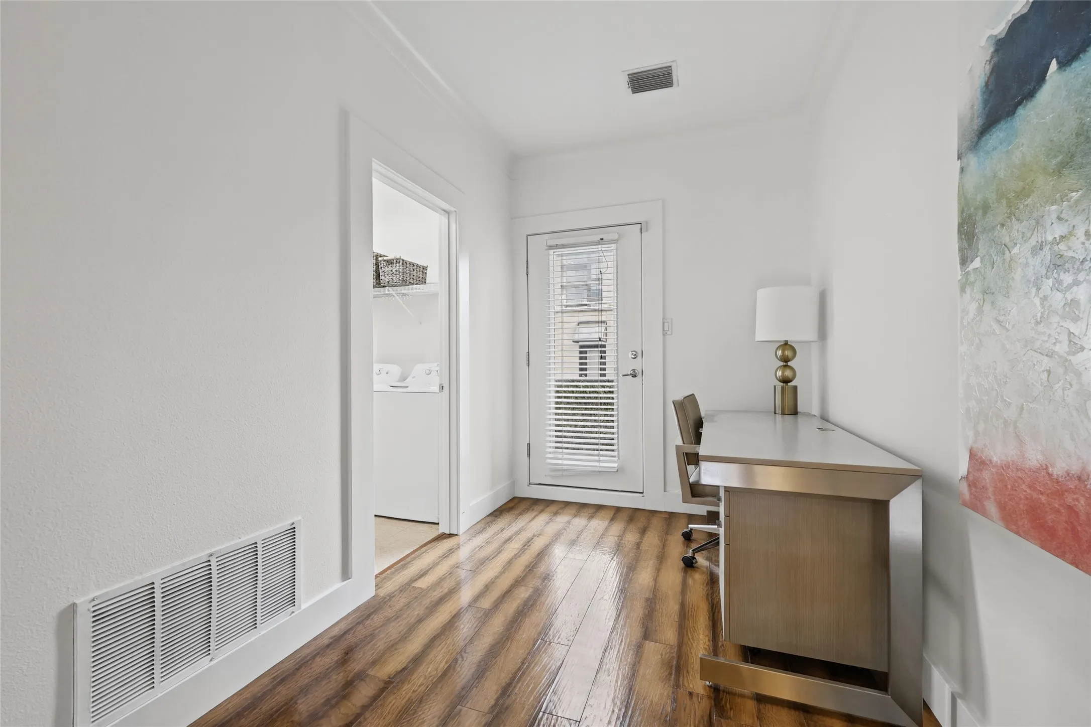 Wood-finish flooring with white baseboards, a white door with blinds, and white walls