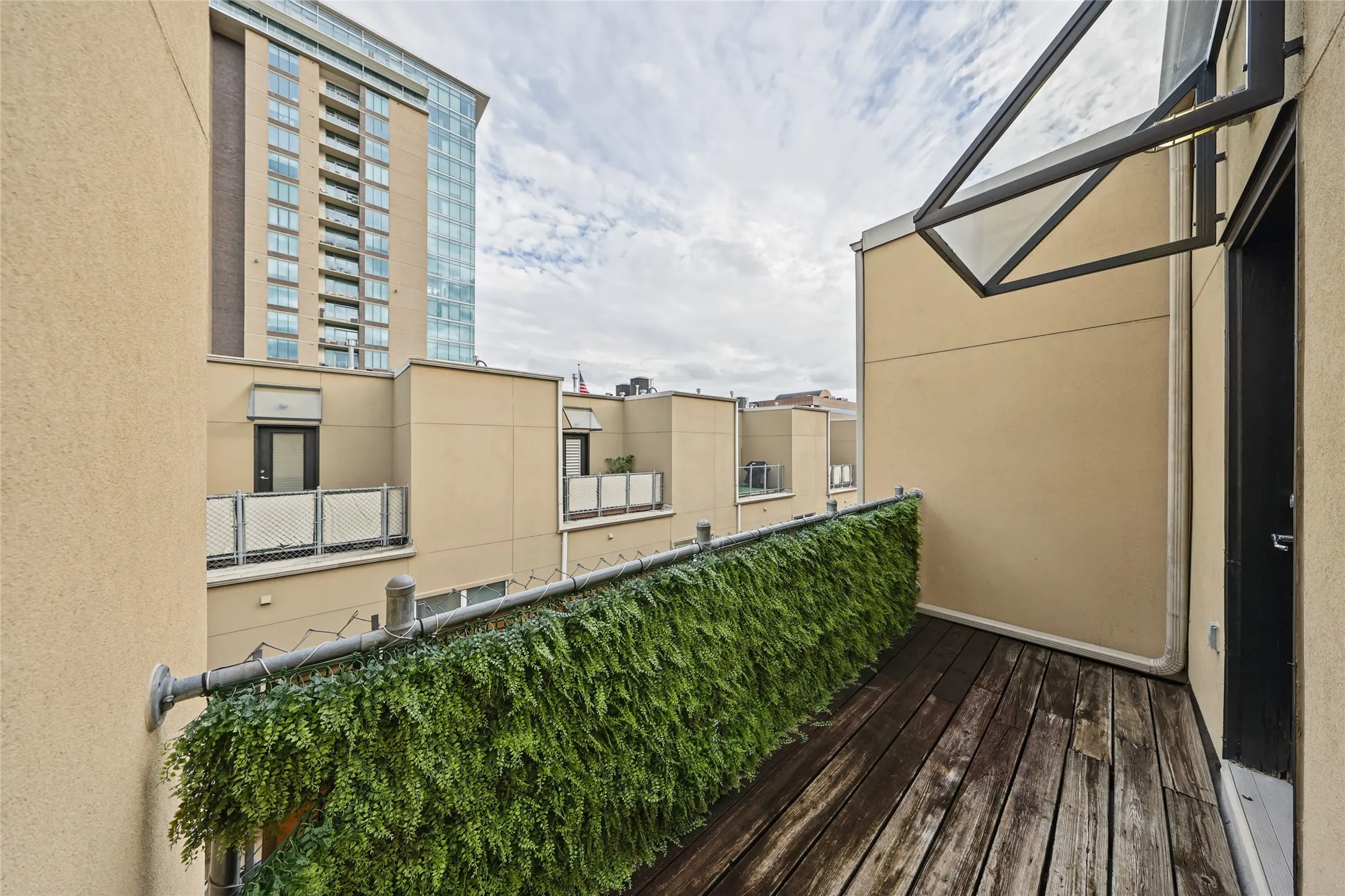 Balcony with wood-finish flooring, a decorative green privacy screen, and a modern glass awning