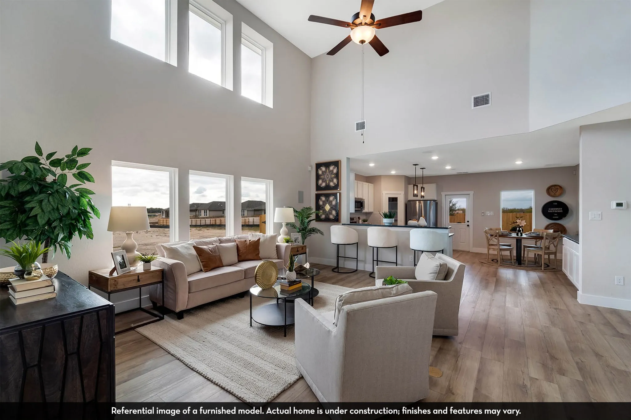 Spacious living area featuring a vaulted ceiling with a ceiling fan, abundant natural light from multiple windows, and wood-finish flooring
