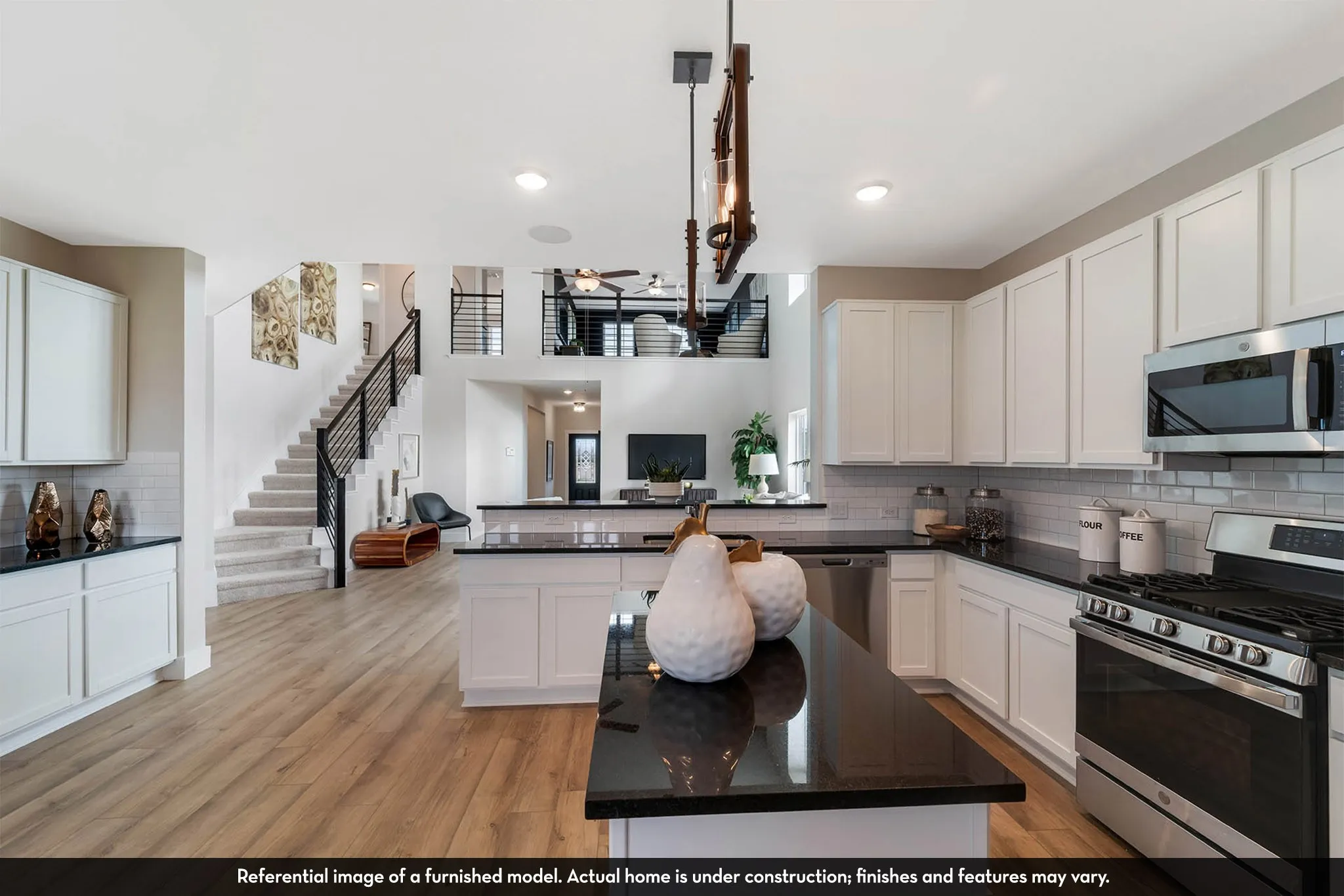 White shaker cabinetry, black countertops, stainless steel appliances, wood-finish flooring, and a staircase with a black metal railing
