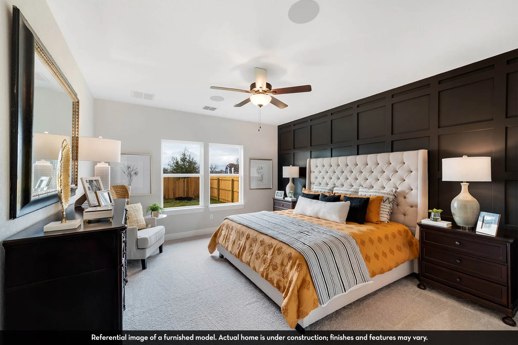 Accent wall with wainscoting, tufted headboard, two windows, ceiling fan, and carpet flooring