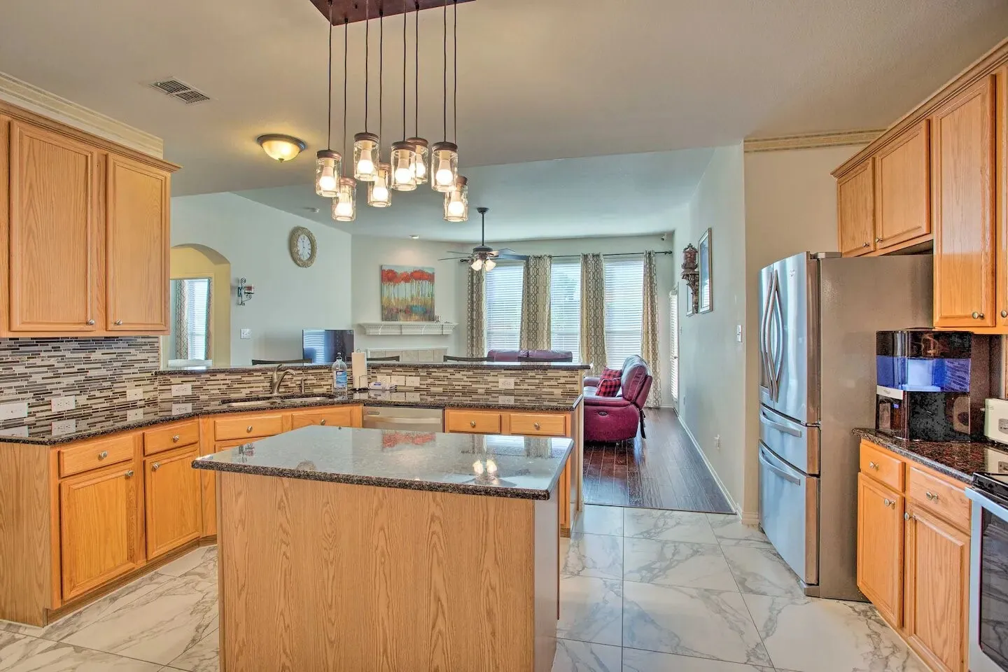 Kitchen featuring wood cabinetry, granite countertops, a mosaic tile backsplash, stainless steel appliances, and an island with pendant lighting