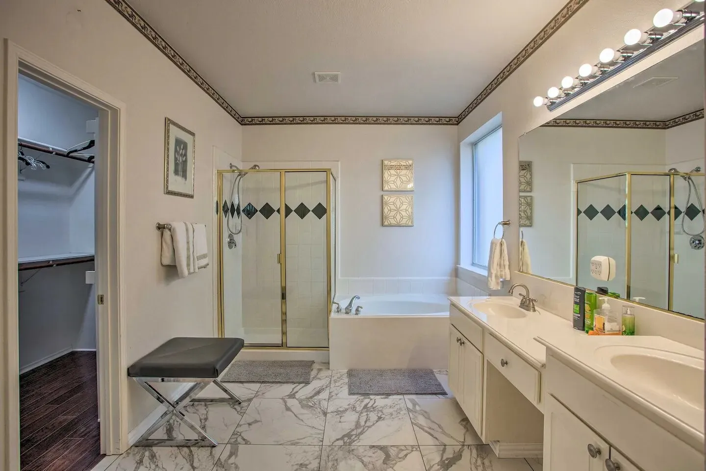 Dual vanity with integrated sinks, a built-in soaking tub, a separate glass-enclosed shower, and marble-finish tile flooring
