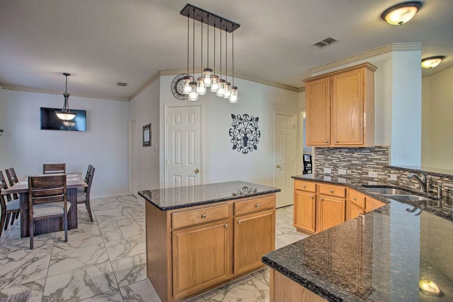 Kitchen featuring wood cabinetry, granite countertops, a decorative tile backsplash, and an island with a pendant light fixture