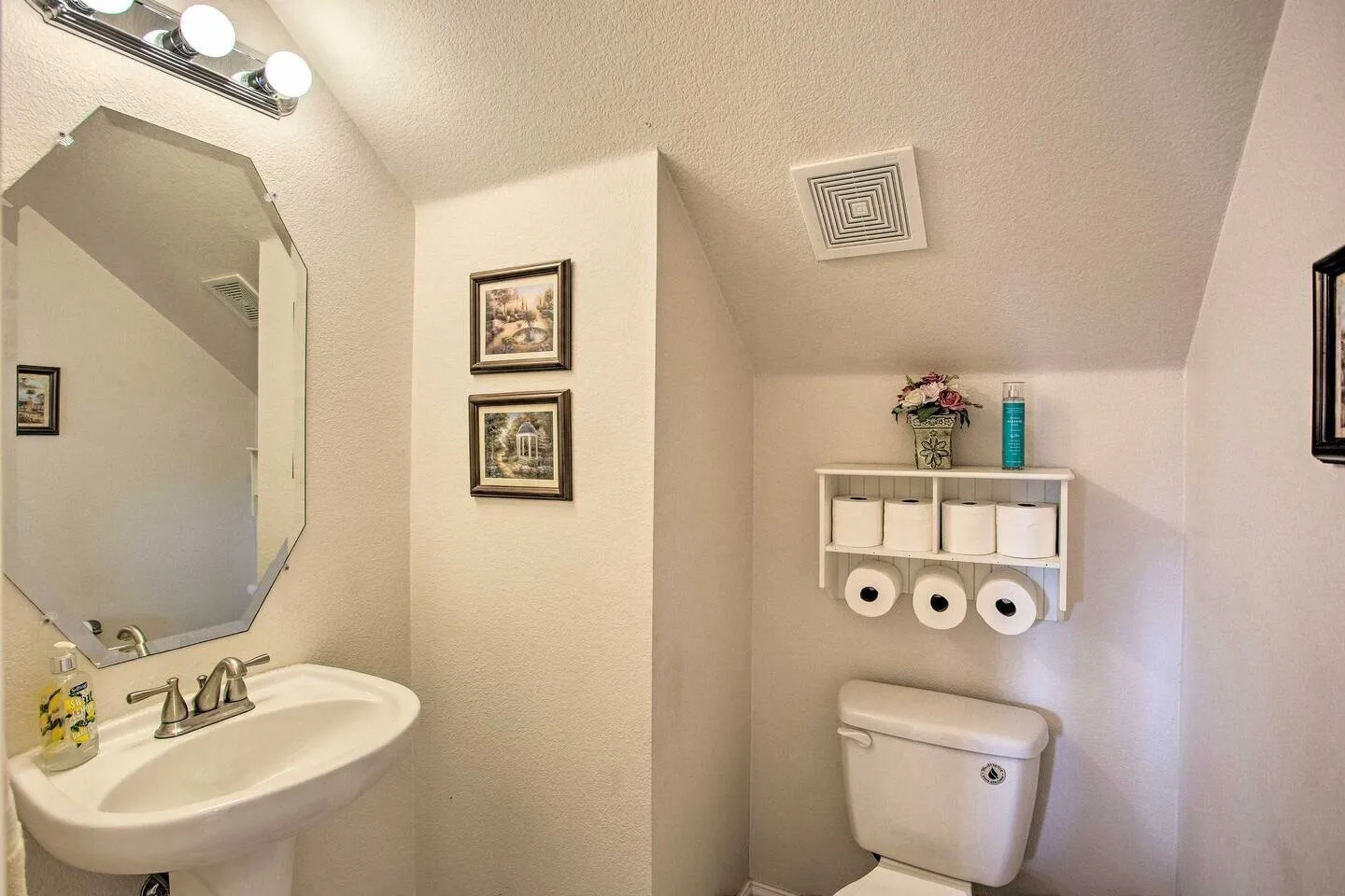 Pedestal sink with brushed nickel faucet, octagonal wall mirror, and vanity lighting