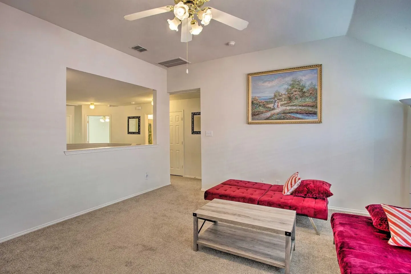 Vaulted ceiling, ceiling fan with integrated lighting, neutral carpet flooring, and a pass-through window opening