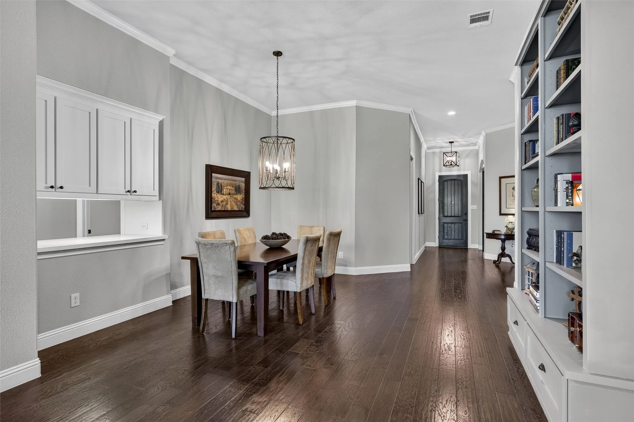 Wood-finish flooring throughout, featuring a built-in buffet with upper cabinetry, a built-in bookcase with lower drawers, and crown molding