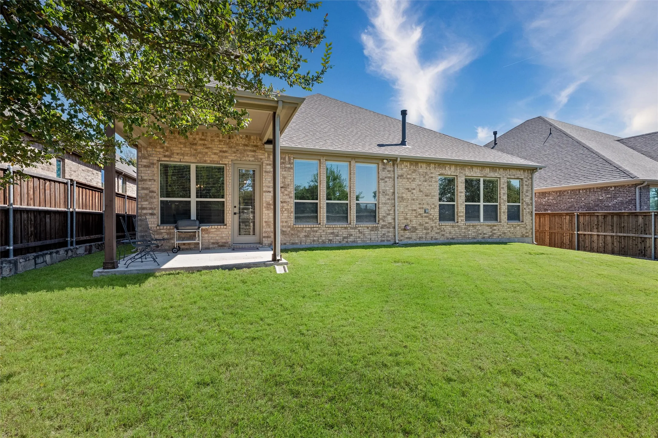 Expansive green lawn with a covered patio, brick exterior, and multiple windows