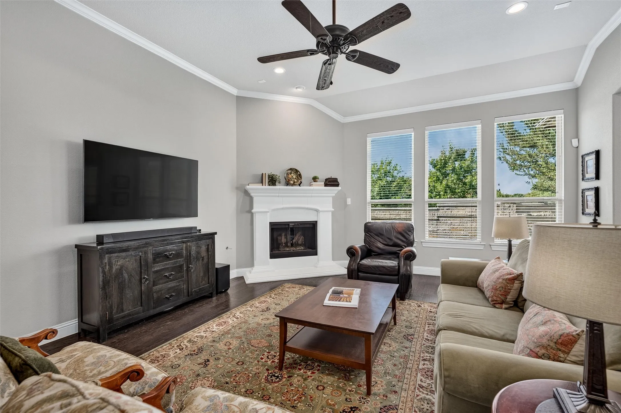 Living area featuring wood-finish flooring, a white mantel fireplace, and three tall windows