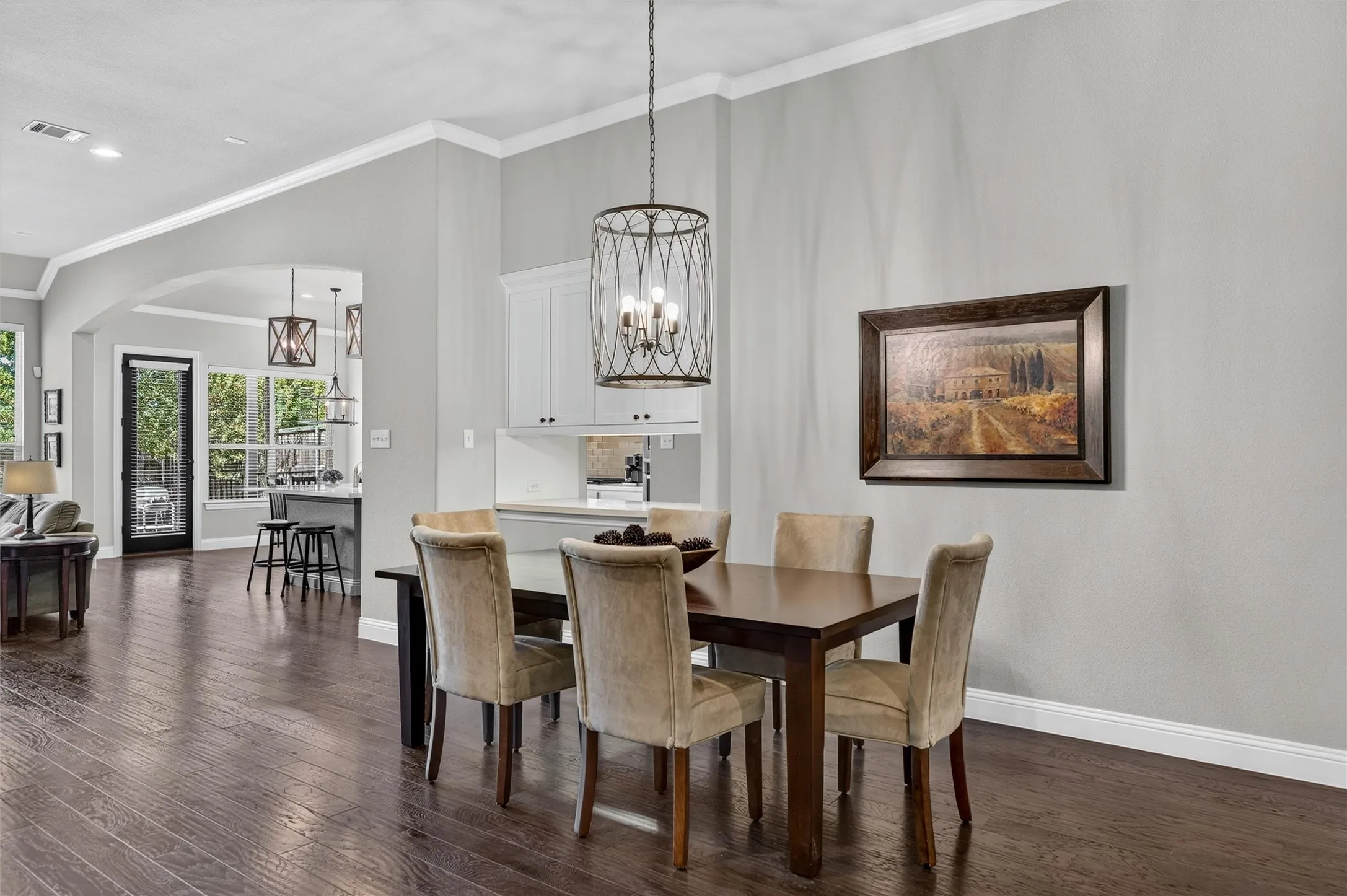 Dark wood-finish flooring, crown molding, arched entryway, white cabinetry, and a drum pendant light fixture