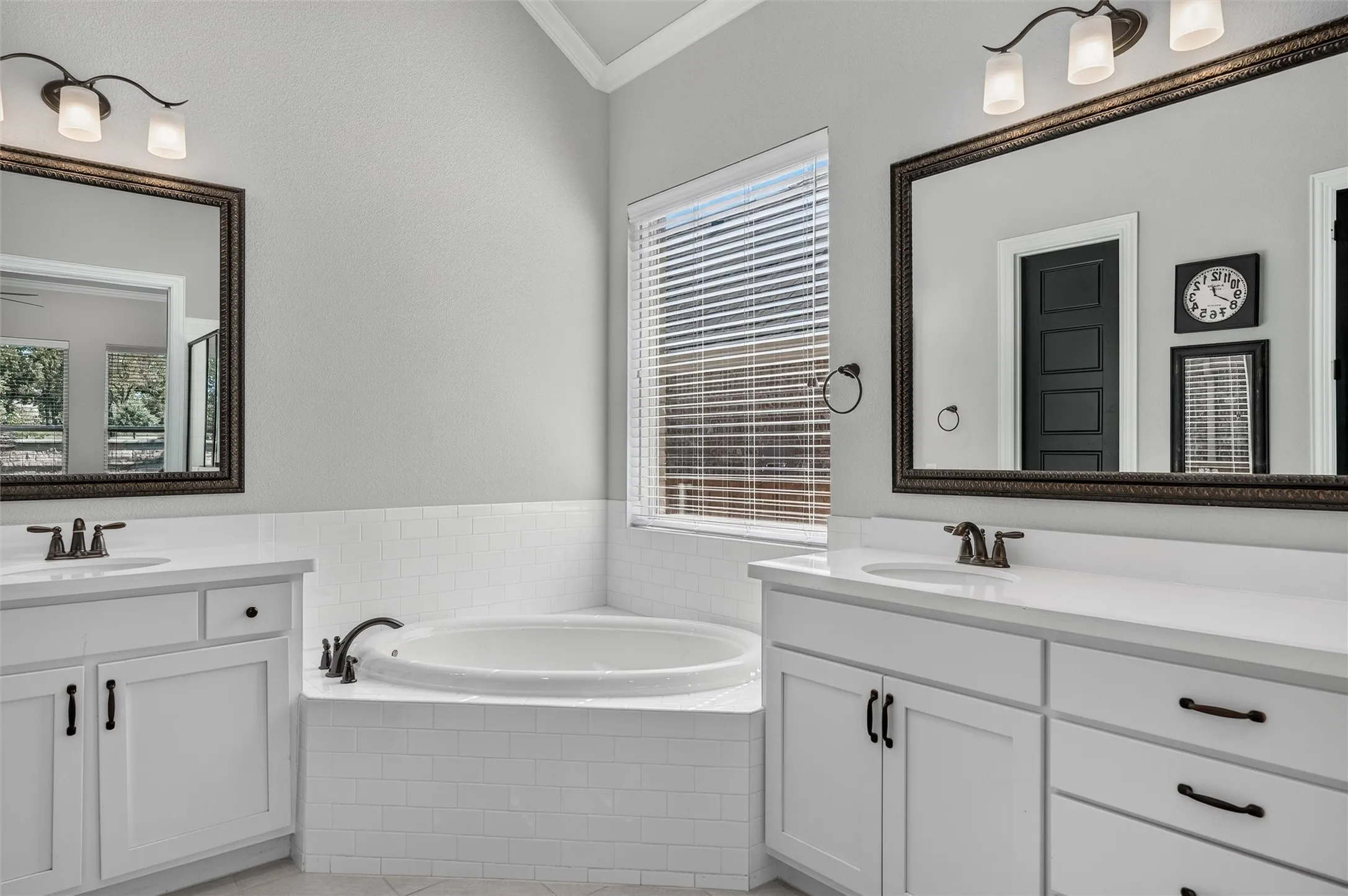 Dual vanity with undermount sinks, white cabinetry, a built-in soaking tub, and subway tile surround