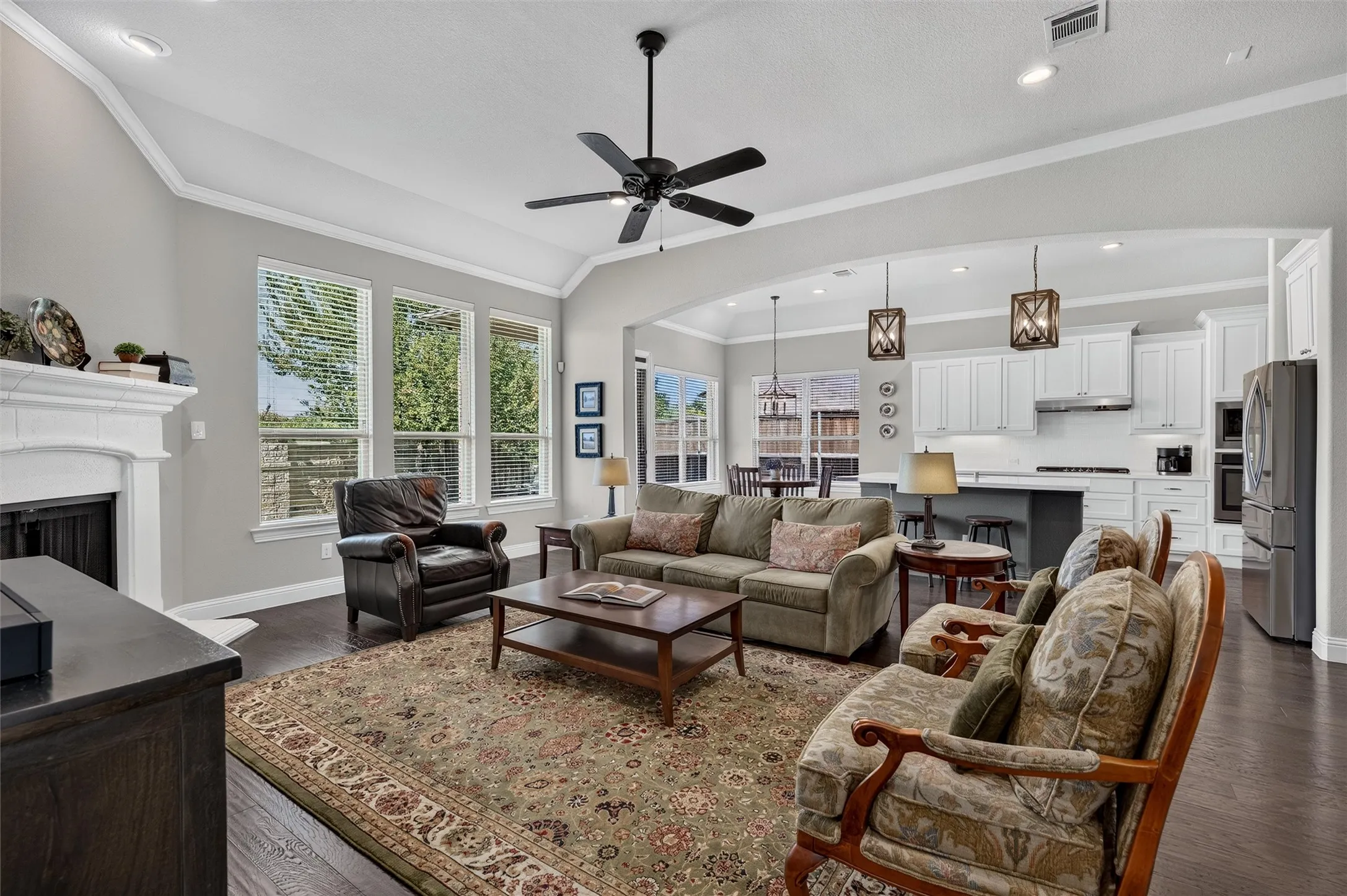 Vaulted ceilings, wood-finish flooring, white cabinetry, integrated stainless steel appliances, and a built-in fireplace with a mantel