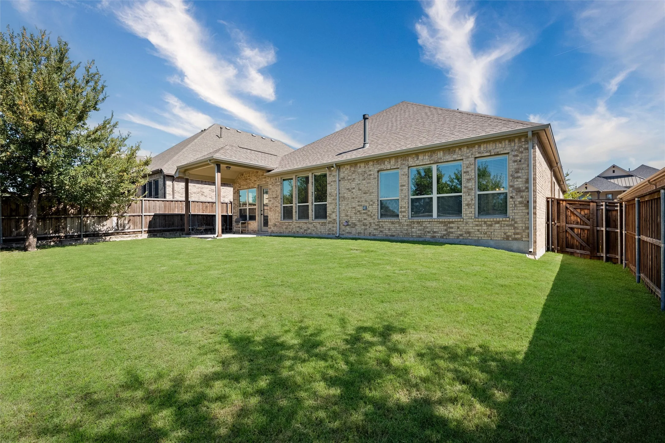 Expansive backyard featuring a manicured lawn, full privacy fencing, and a covered patio