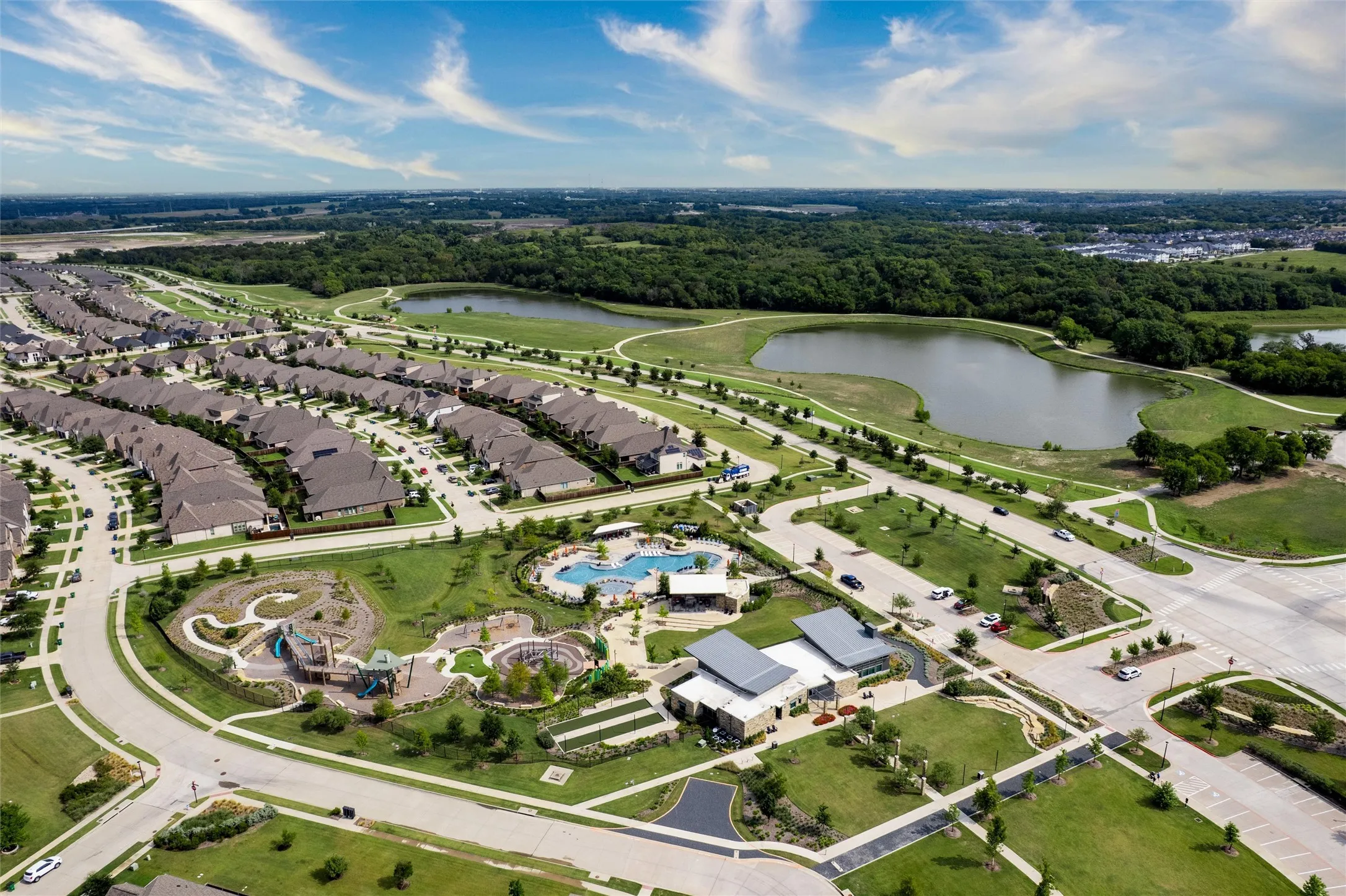 Aerial perspective showcasing the community layout with residential properties, a large central park, a swimming pool, and natural water features