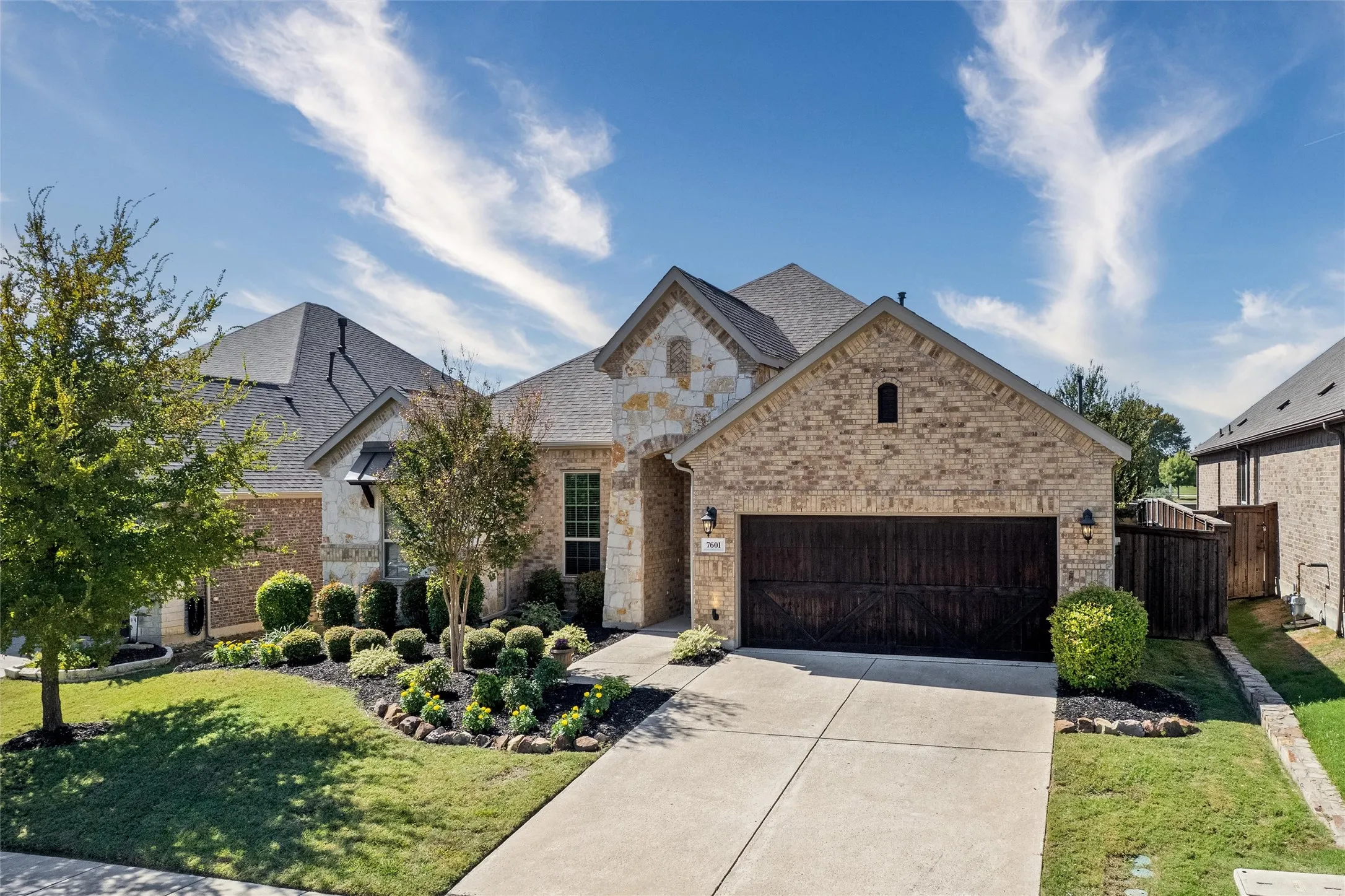 Brick and stone exterior with an attached garage, concrete driveway, and established front landscaping